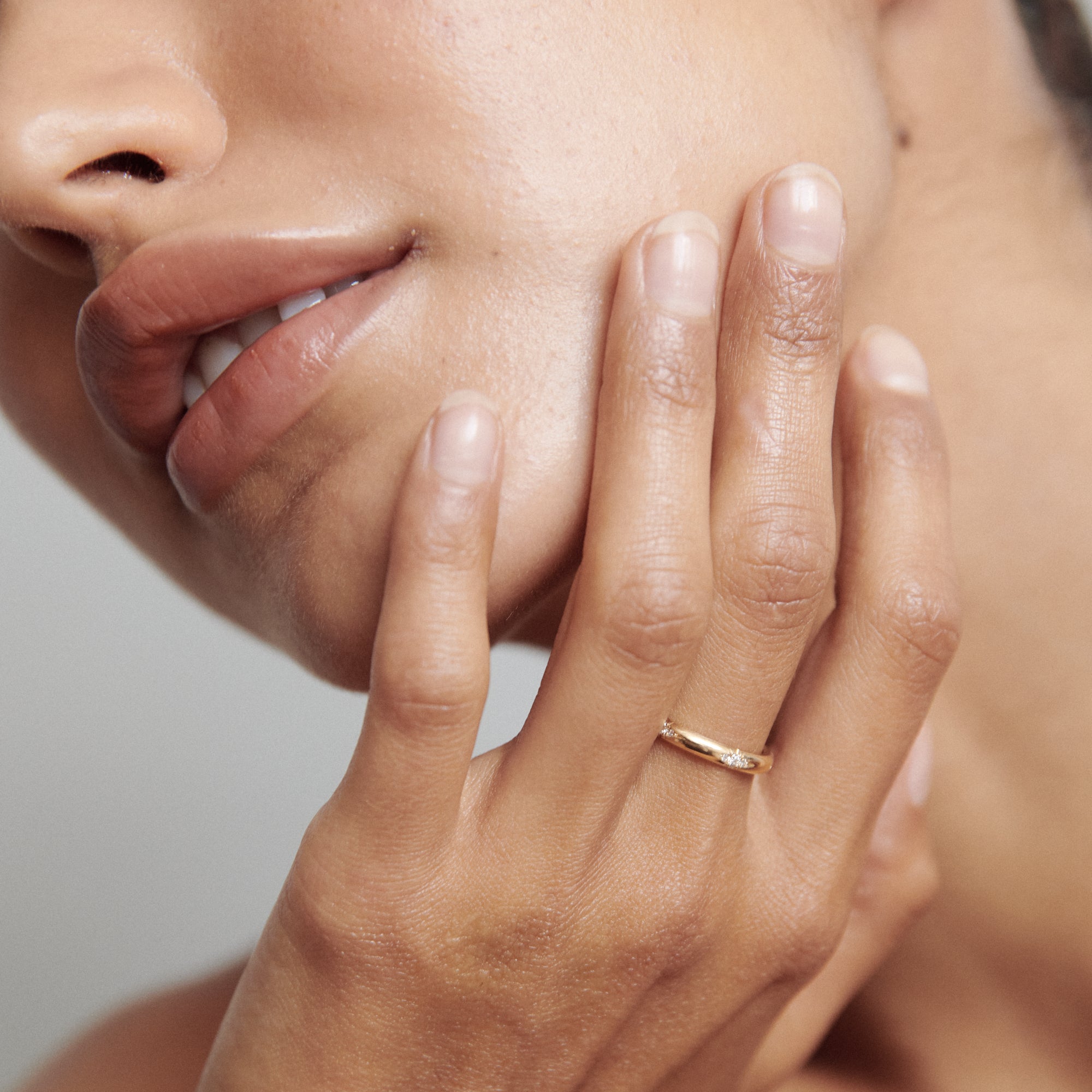 Close-up of a hand with manicured nails, delicately holding the chin. The person wears a sleek gold ring, showcasing elegant jewellery style.