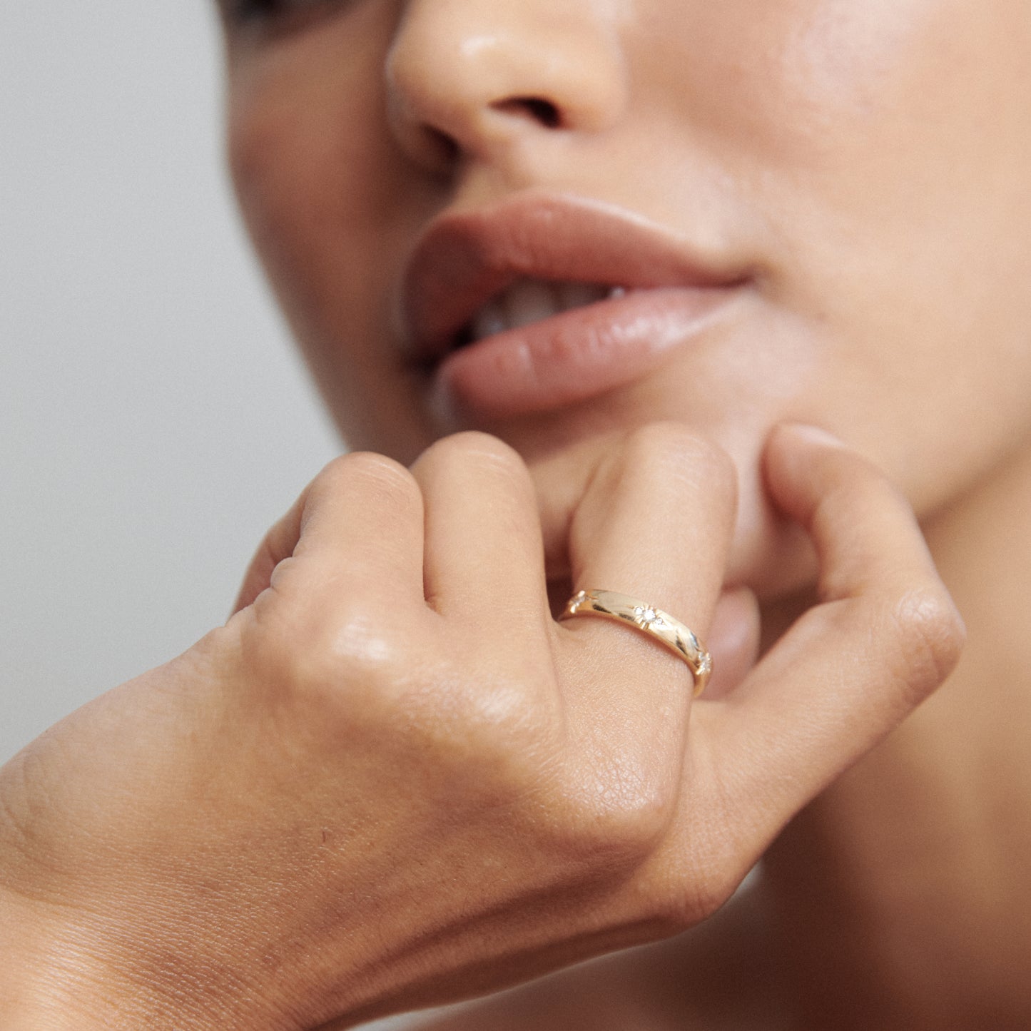 Close-up of a person wearing an elegant gold ring, their lips gently parted. Luxurious jewellery style showcasing fine craftsmanship.