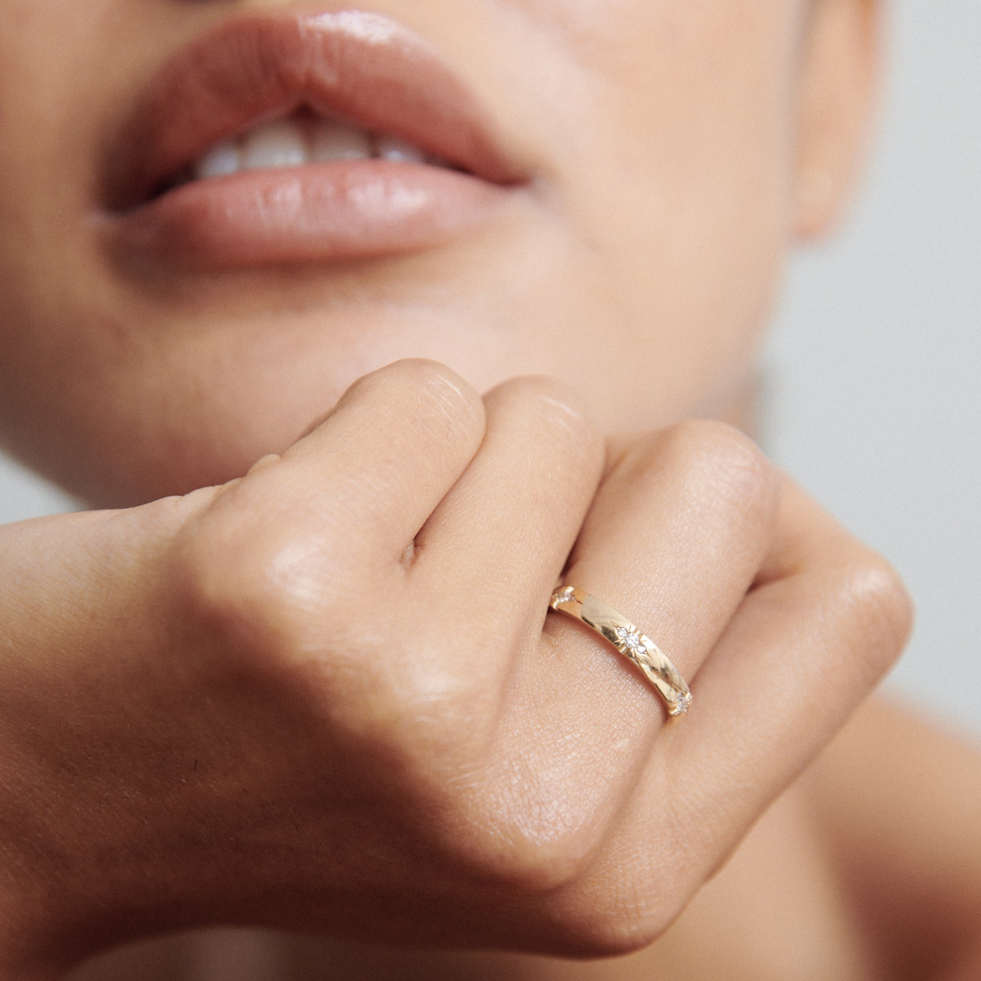 Close-up of a person wearing a textured gold ring on their finger. Their lips are visible, providing contrast to the luxurious jewellery piece.