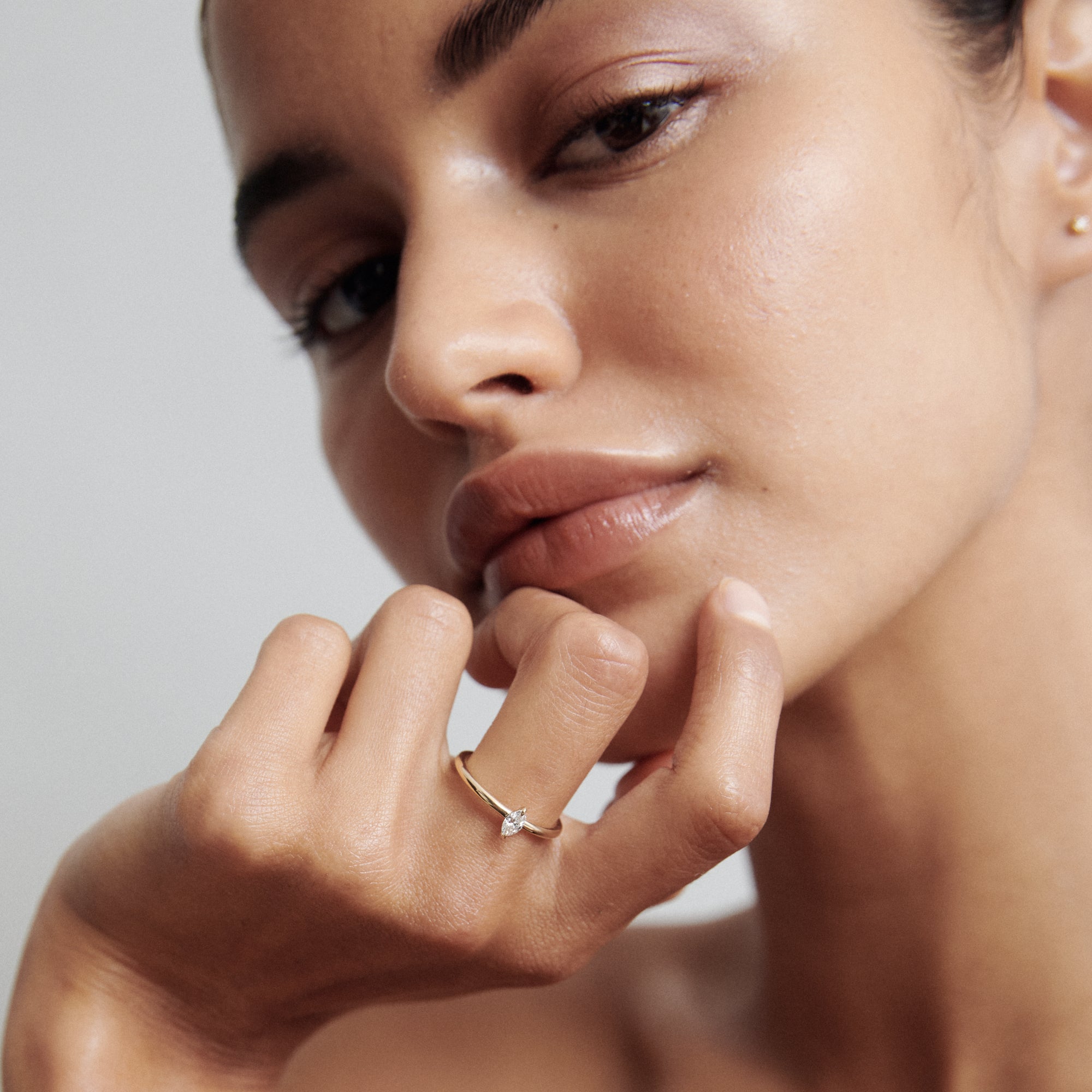Woman's face close-up showcasing a delicate gold ring with a small diamond, emphasising luxury jewellery and minimalist elegance.