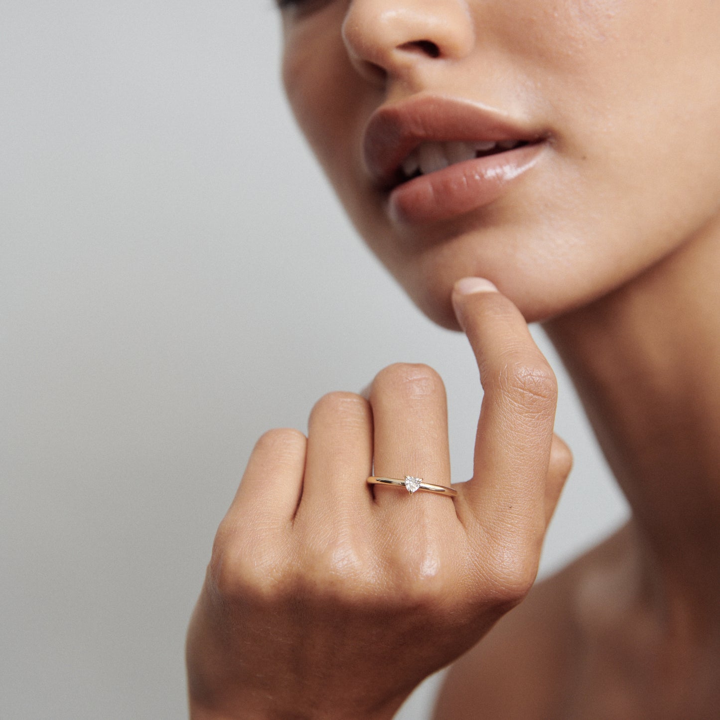 Woman's hand with elegant gold solitaire ring near her lips, soft lighting, luxury jewellery focus.