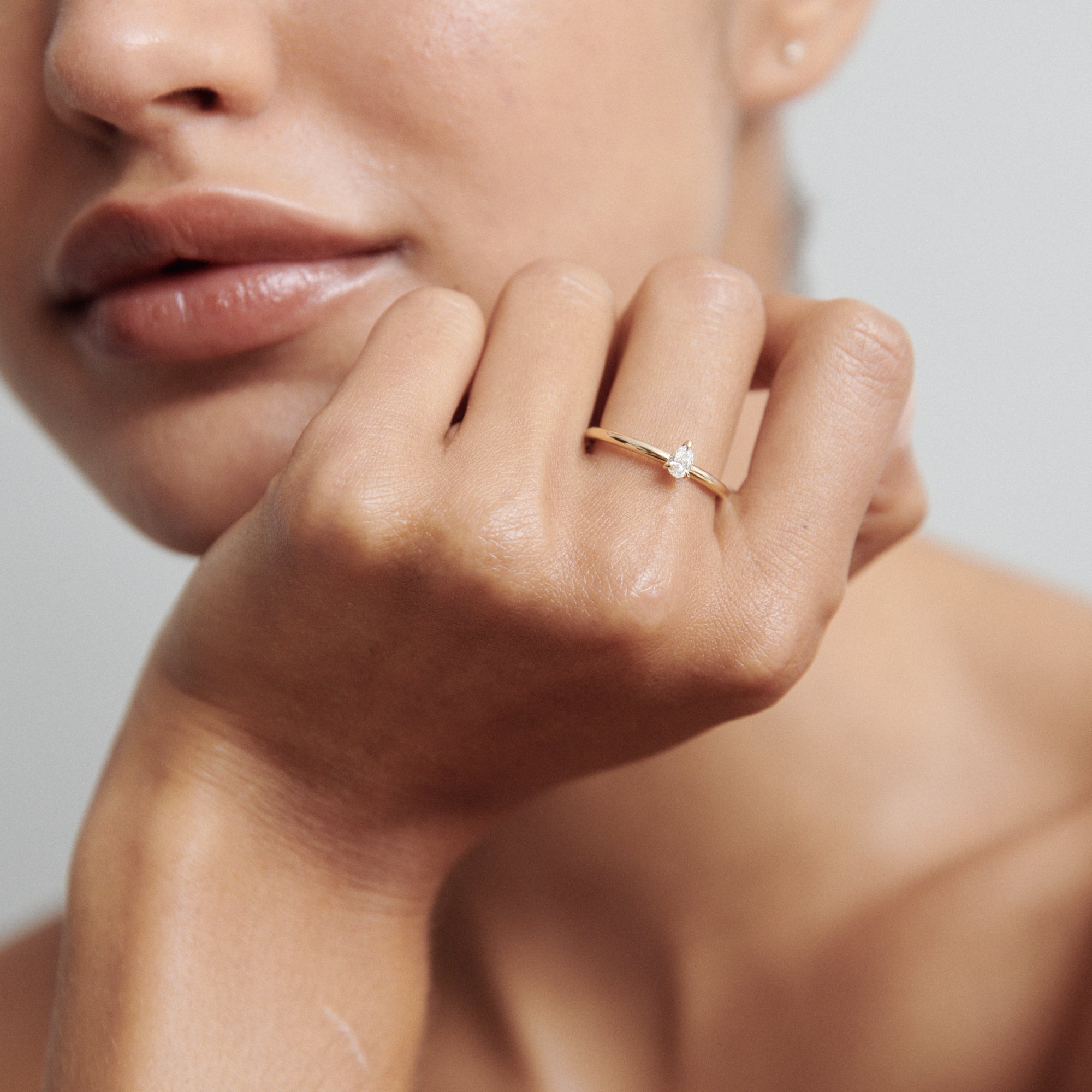 Close-up of a woman's hand wearing a delicate gold ring with a small diamond, against a blurred background. Luxury jewellery photography.