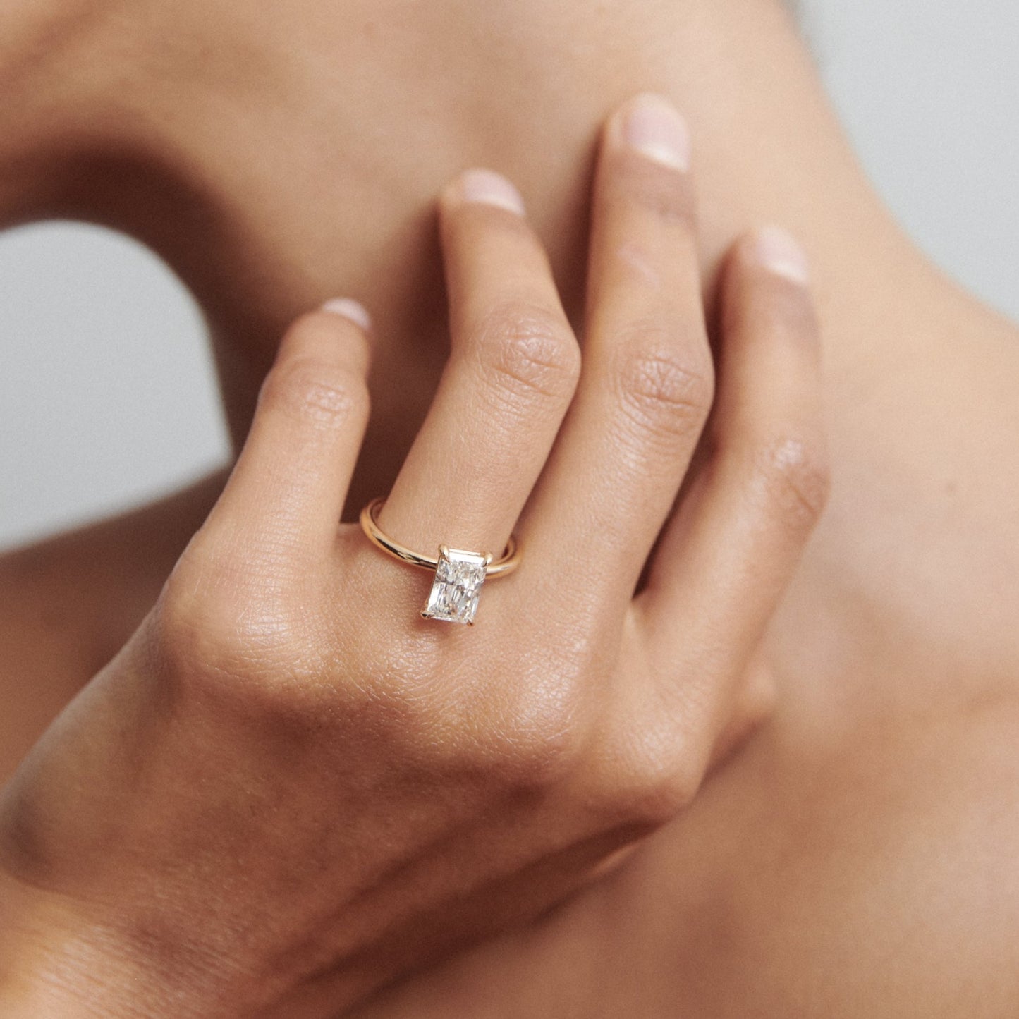 Woman's hand showcasing a gold ring with a radiant cut diamond, elegantly posed near neck. Luxury jewellery detail.