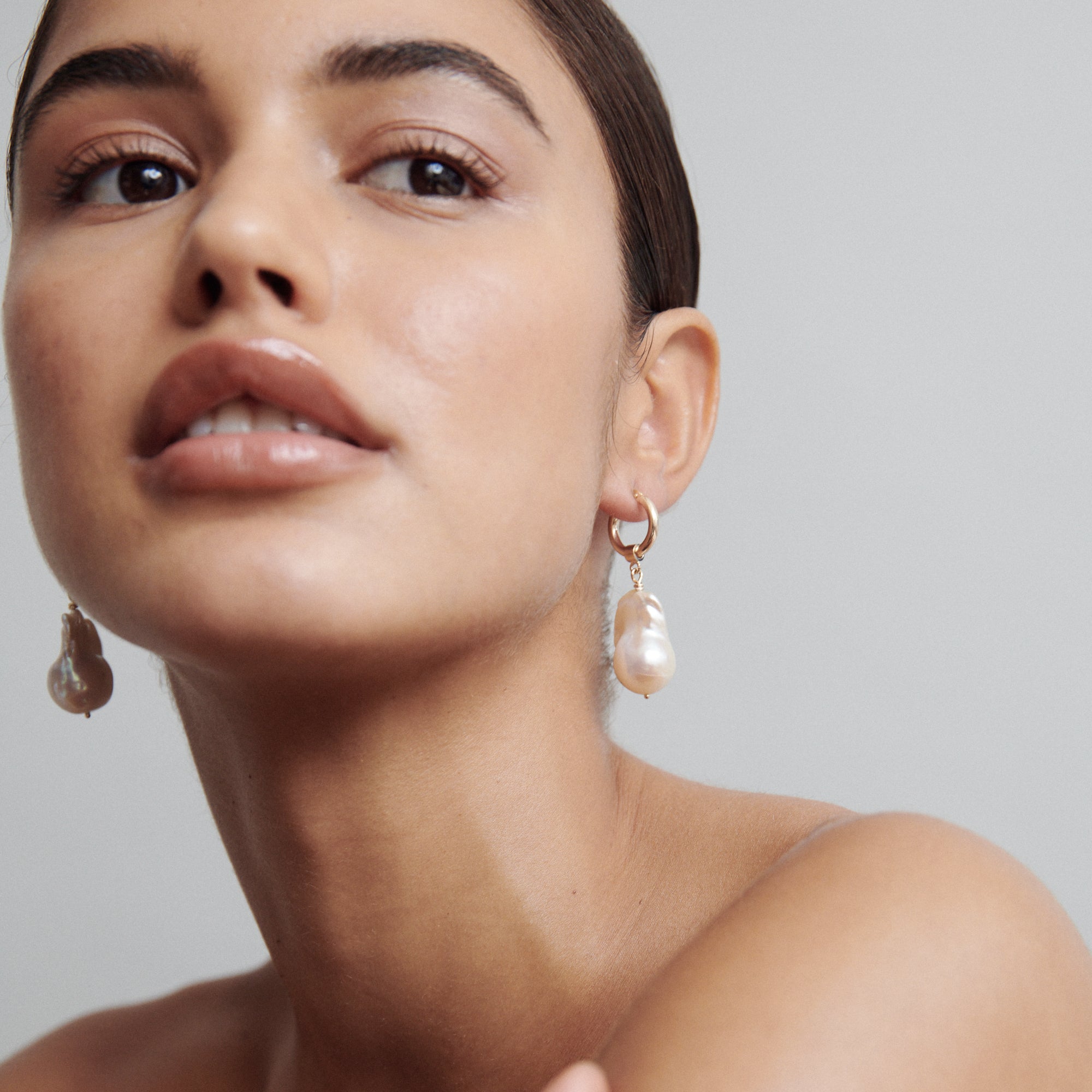 Woman wearing elegant gold and pearl drop earrings, highlighting luxury jewellery against a soft, neutral background.