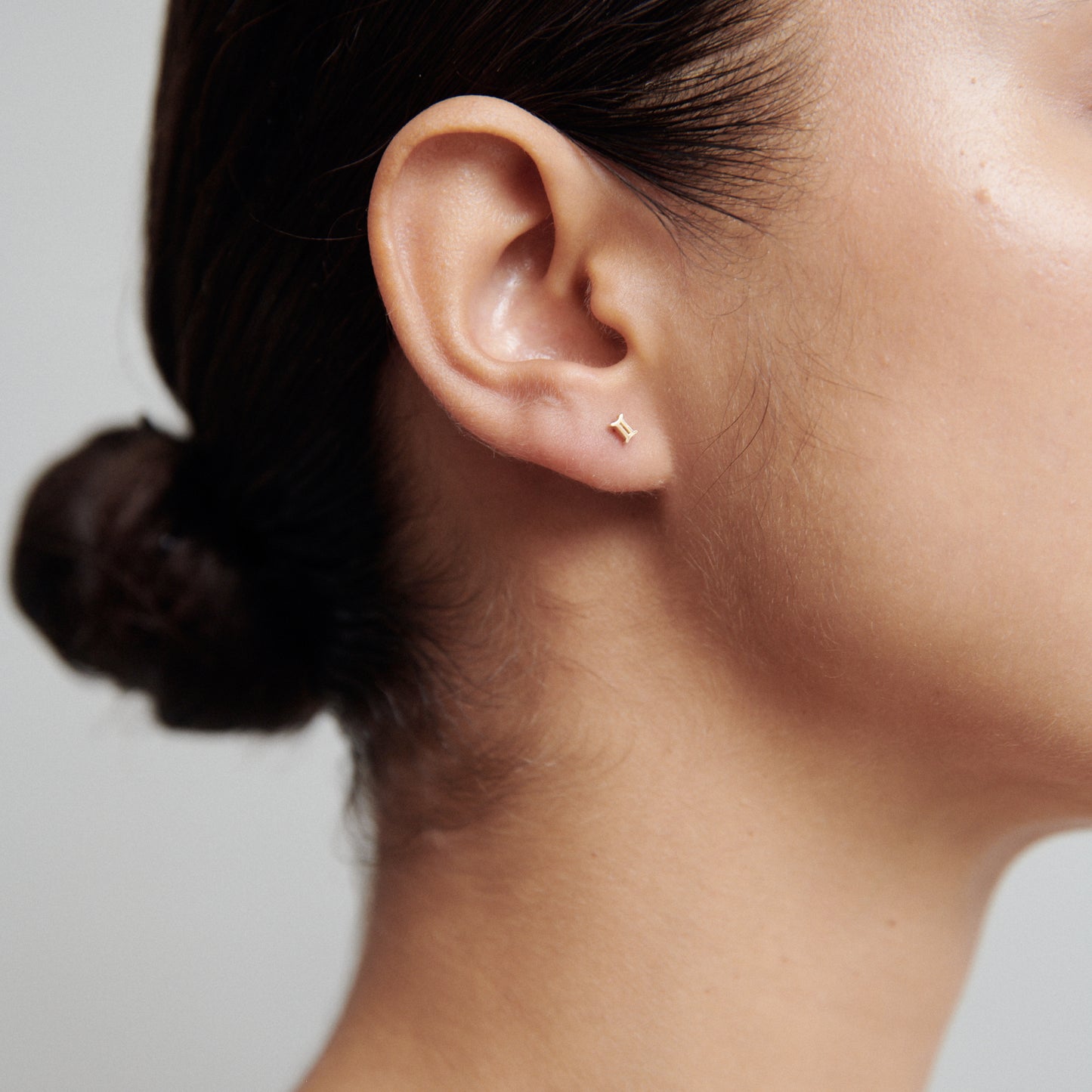 Close-up of a woman's ear with a minimalist gold star stud earring. Hair tied back, showcasing luxury jewellery elegance.