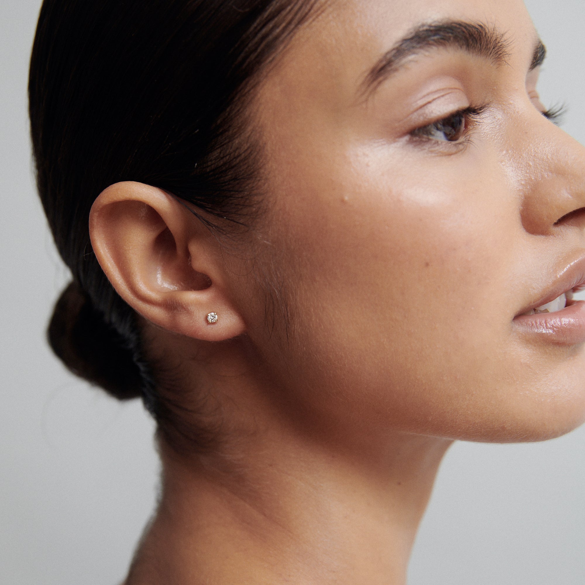 Close-up of a woman wearing a single small diamond stud earring. Her hair is neatly pulled back, showcasing the jewellery elegantly.