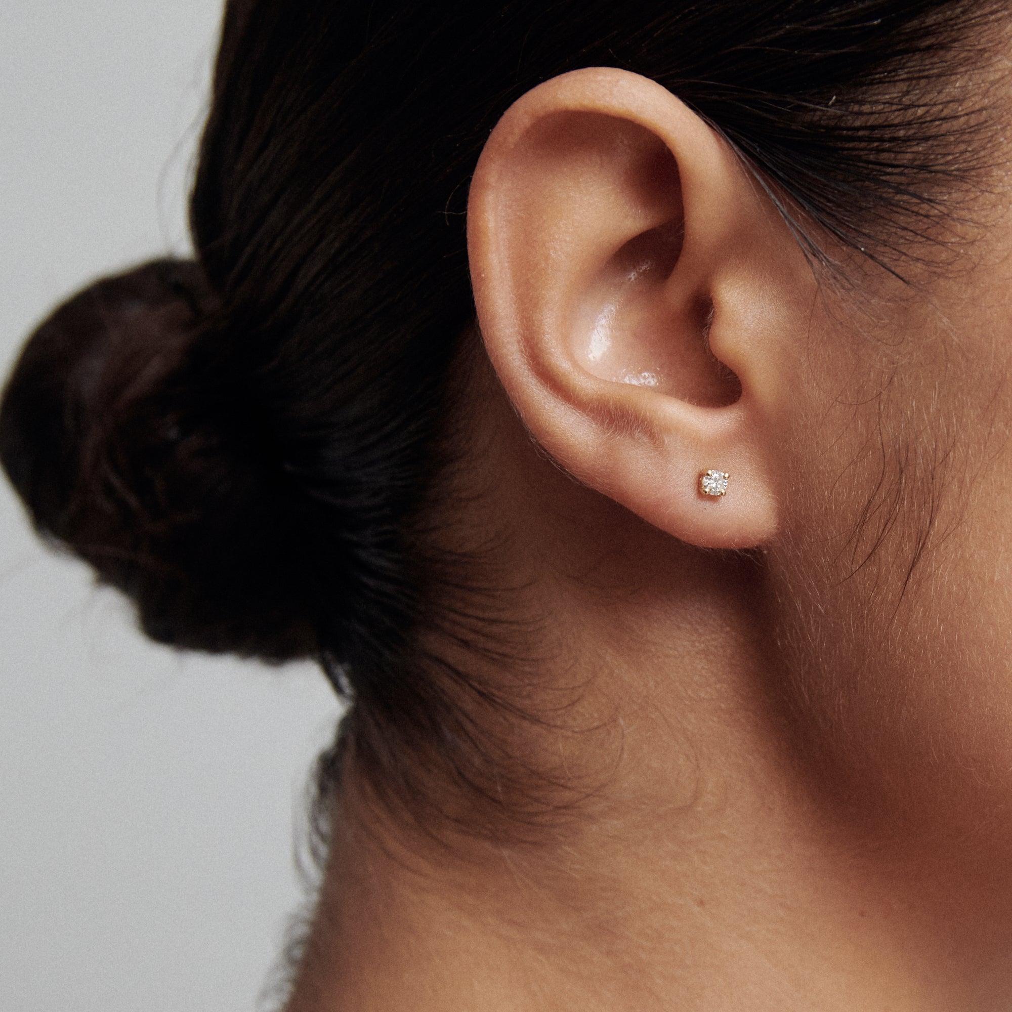 Close-up of a woman's ear adorned with a single elegant diamond stud earring, showcasing luxury jewellery style.