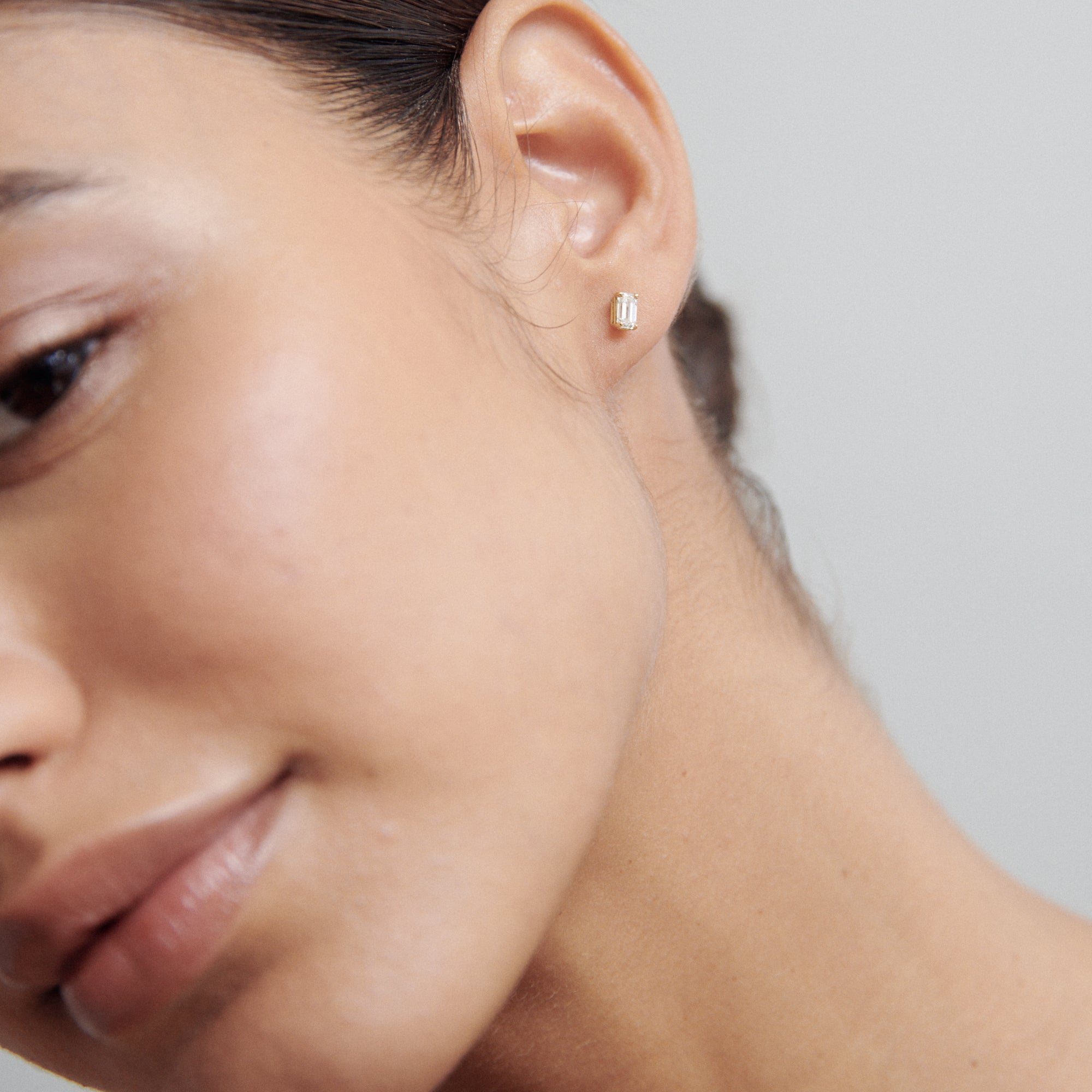 Close-up of a woman wearing a sleek, gold stud earring against a neutral background. Luxurious jewellery detail, modern elegance.