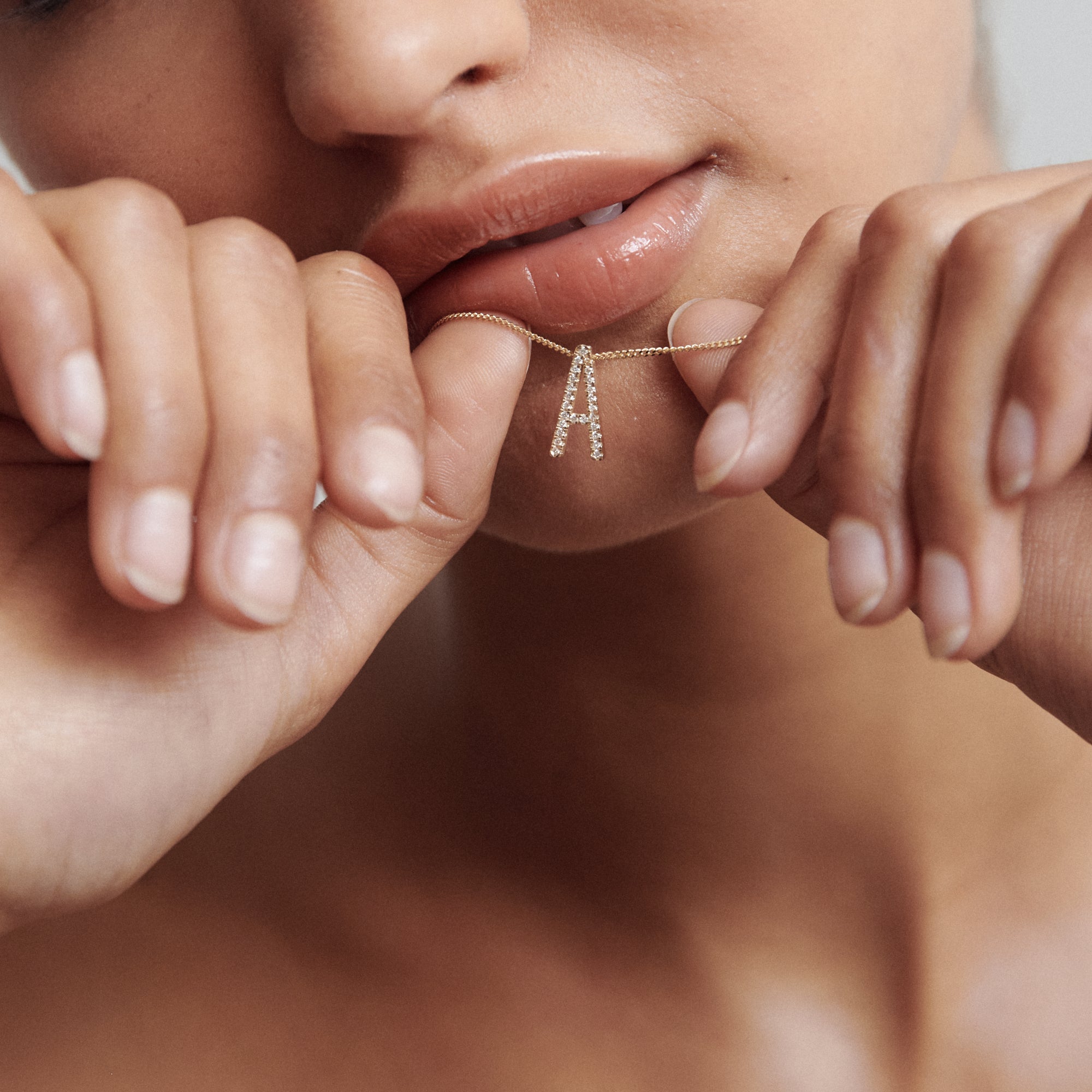 Woman gently holding a delicate gold necklace between her fingers, featuring a small, diamond-studded pendant, near her lips.