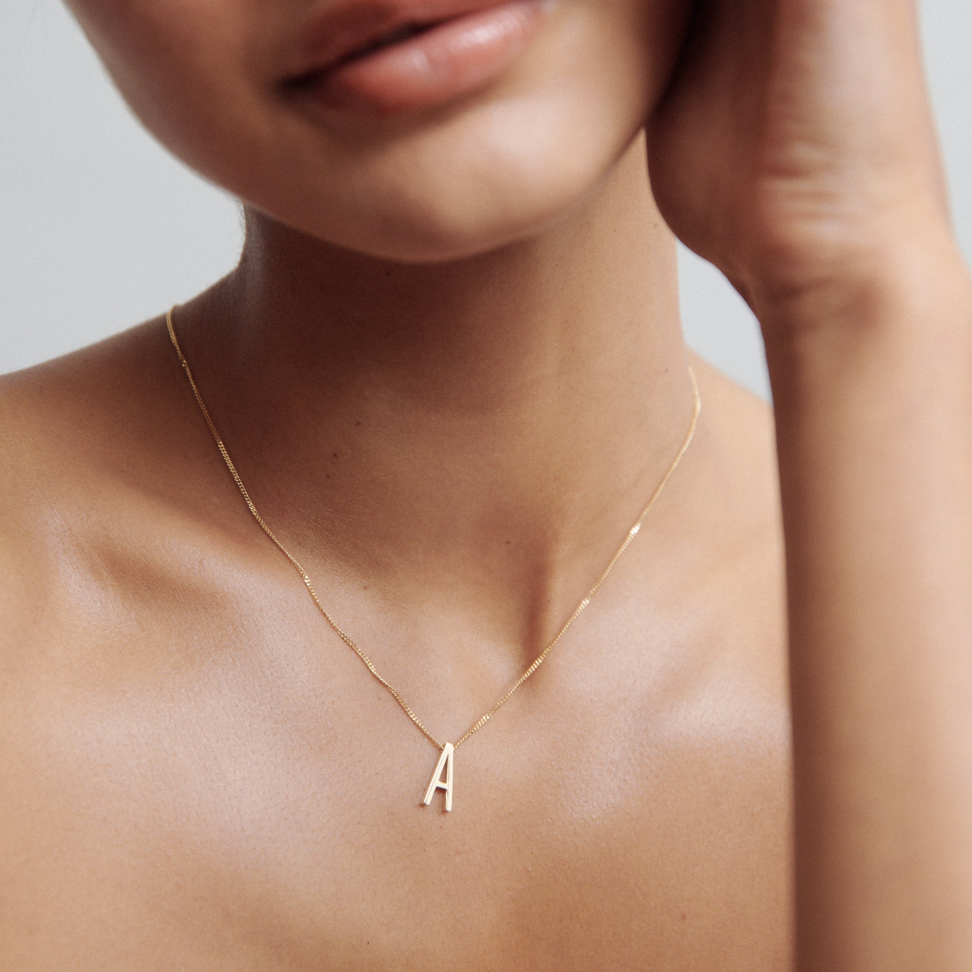 Close-up of a woman wearing a delicate gold necklace with an 'A' pendant, showcasing minimalist luxury jewellery.