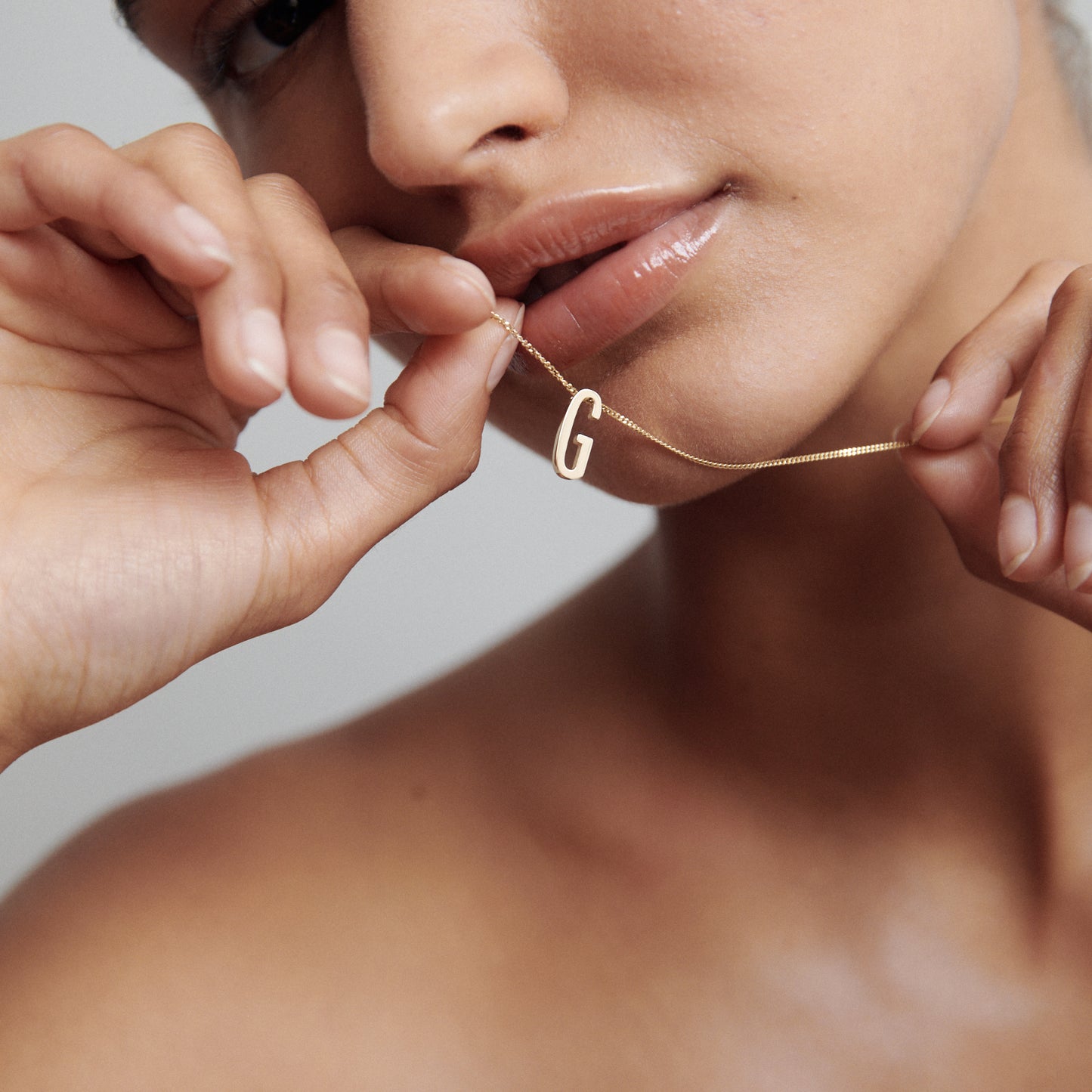Close-up of a woman holding a gold necklace with a “G” pendant near her lips, highlighting luxury jewellery and elegant design.