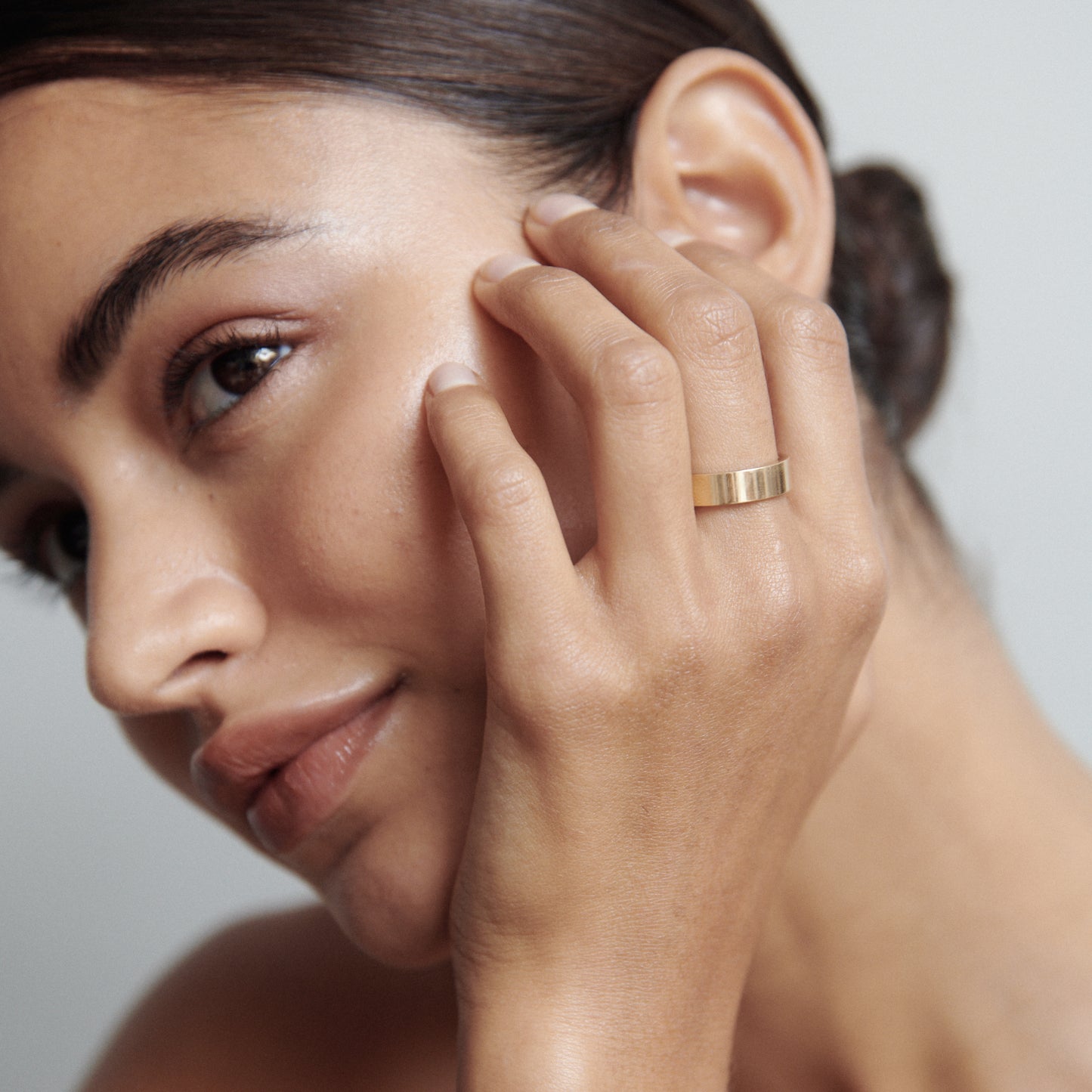 Woman wearing a sleek gold ring, touching her face. The ring stands out against her smooth complexion, highlighting luxury jewellery elegance.