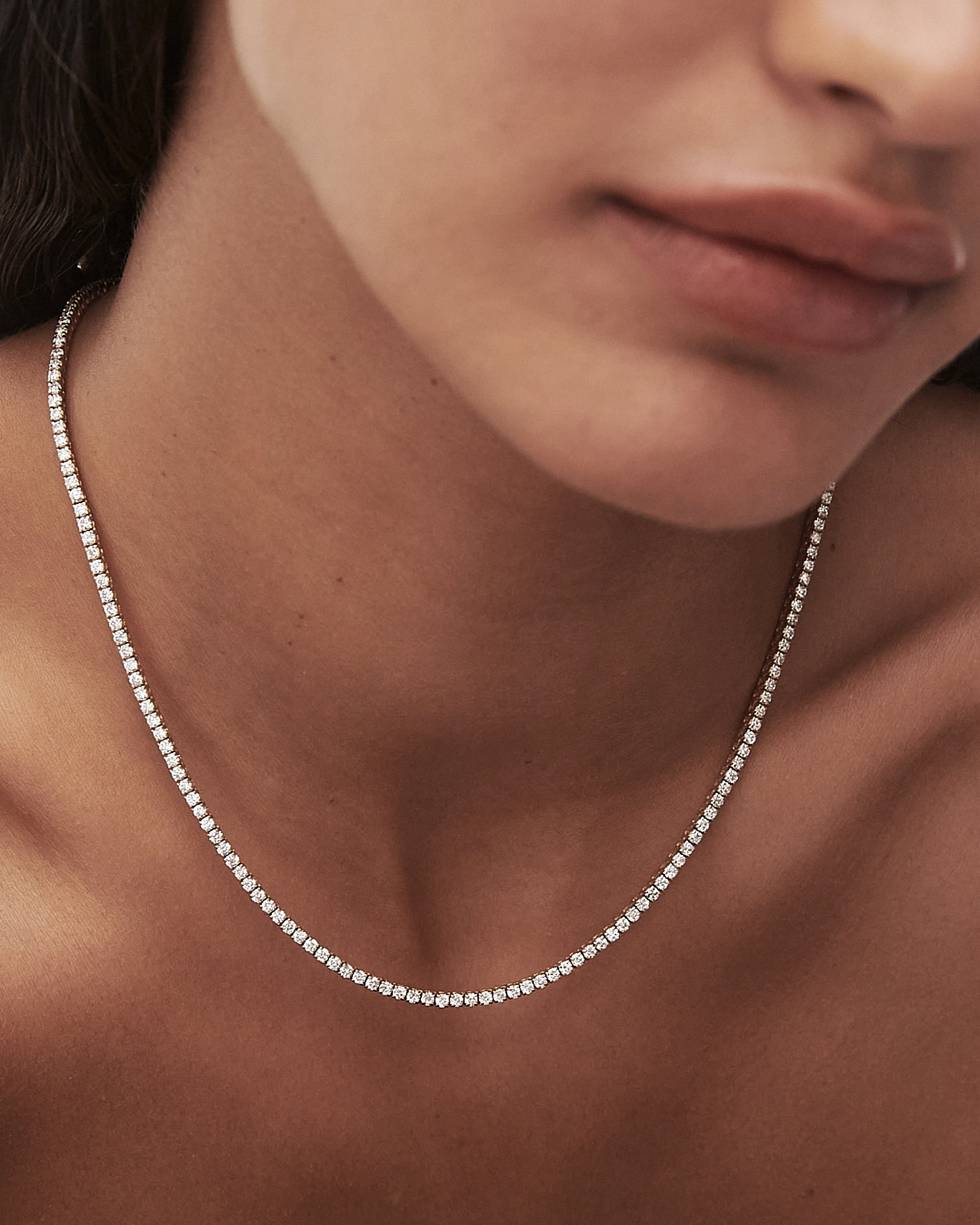 Close-up of a woman's neck wearing an elegant diamond tennis necklace, showcasing luxury jewellery with soft lighting.