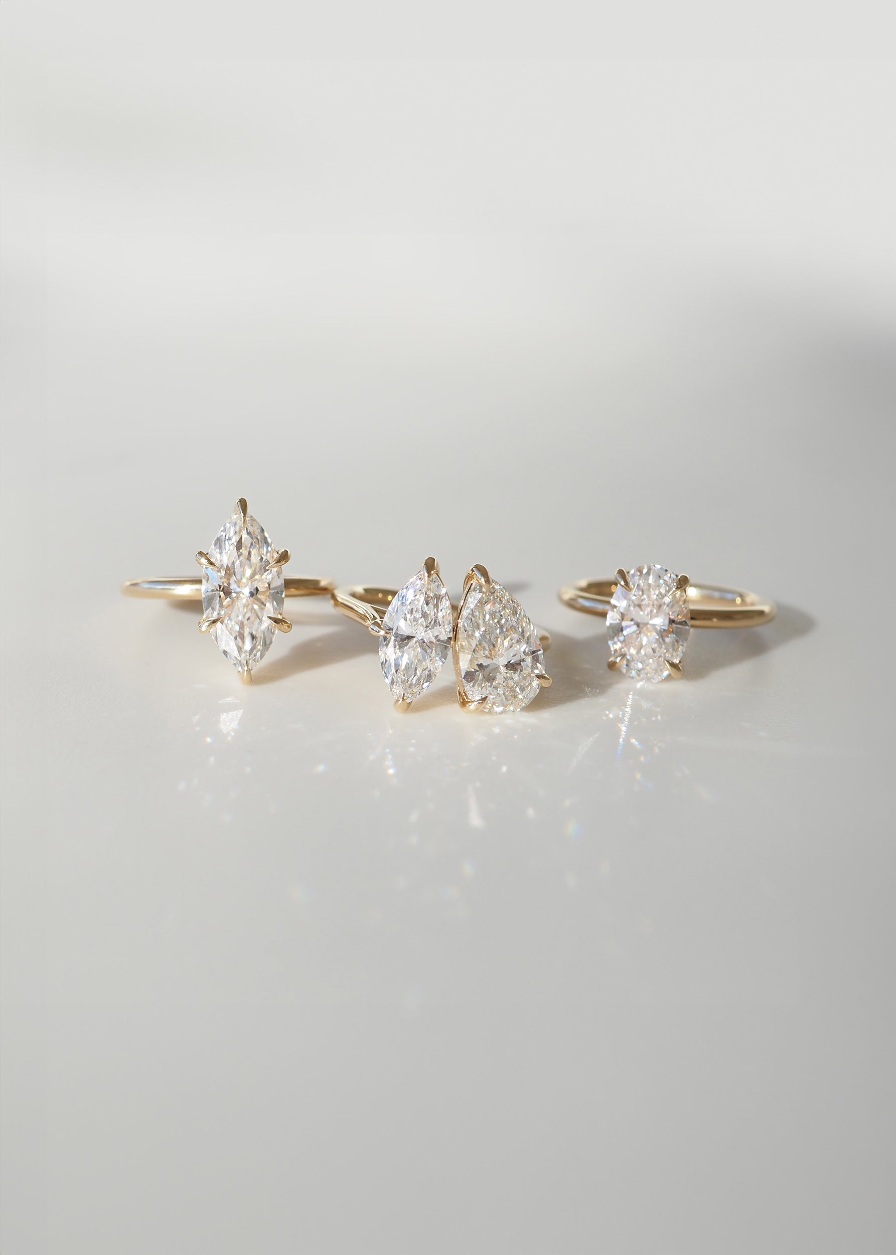 Four gold rings with marquise, pear, and oval-cut diamonds on a reflective surface, elegantly showcasing luxury jewellery design.