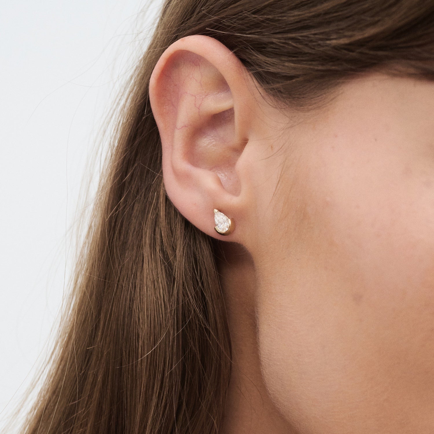 Close-up of a woman's ear wearing a teardrop-shaped diamond stud earring, set in gold, exuding luxury and elegance.
