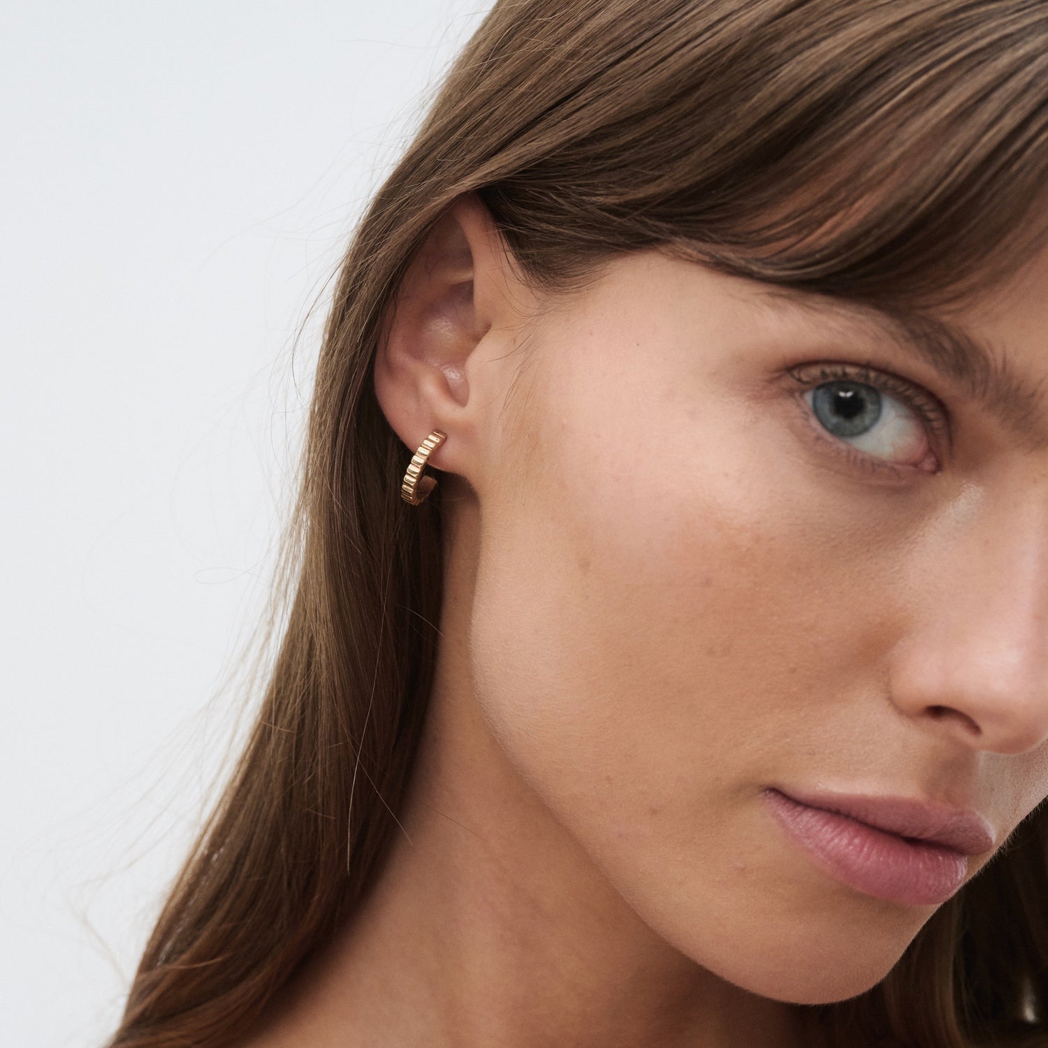 Close-up of a woman wearing a small gold hoop earring with diamonds, showcasing luxury jewellery against a neutral background.