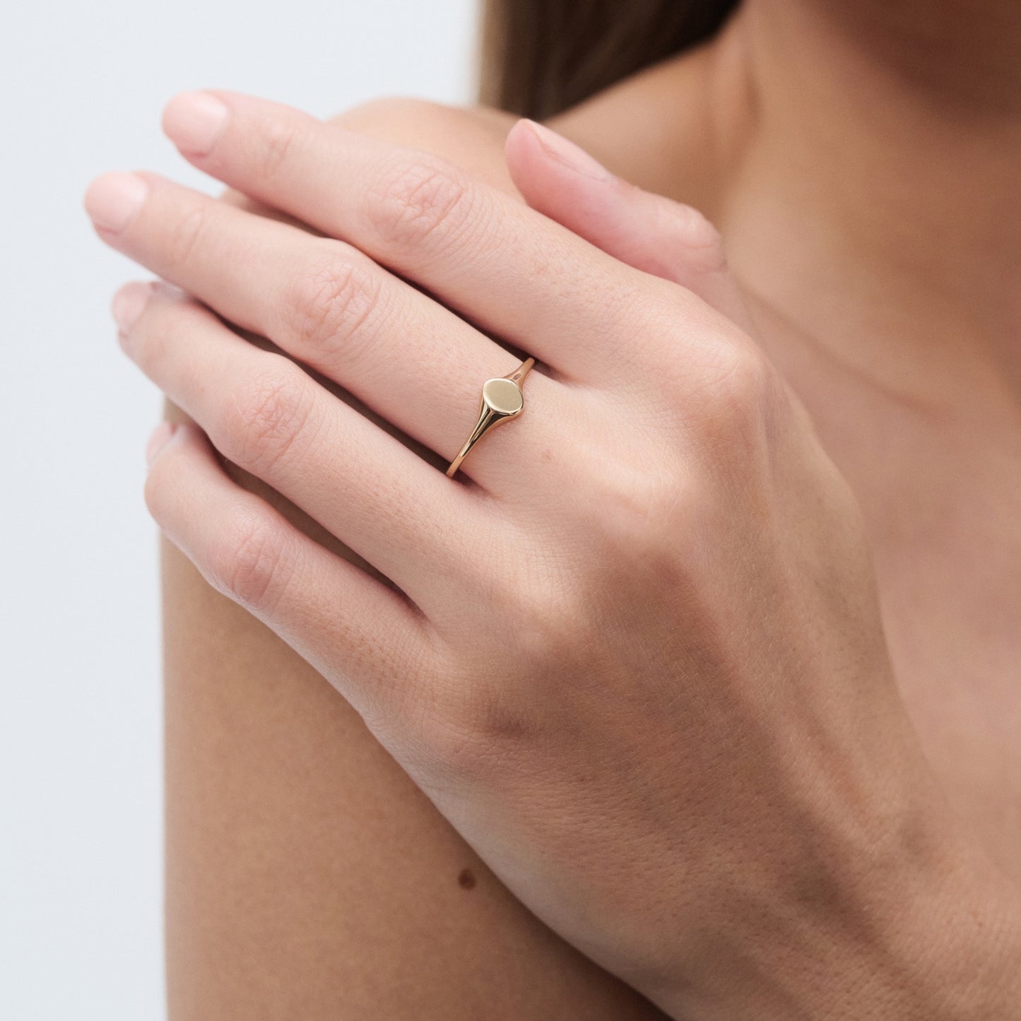 Close-up of a woman's hand wearing a delicate gold ring with a small heart-shaped design, set against a light background.