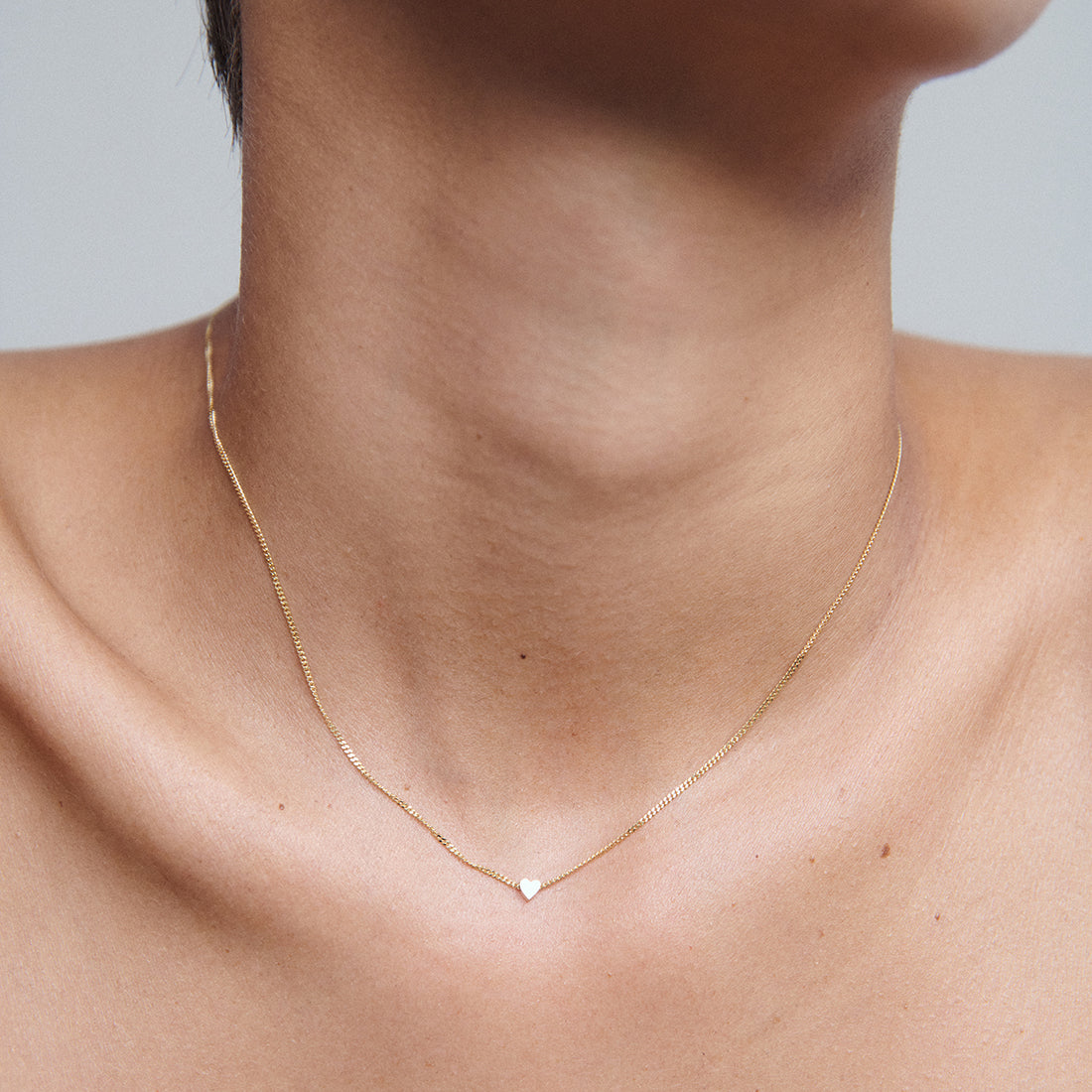 Delicate gold chain necklace with tiny heart pendant on a woman's neck, showcasing minimalist luxury jewellery.