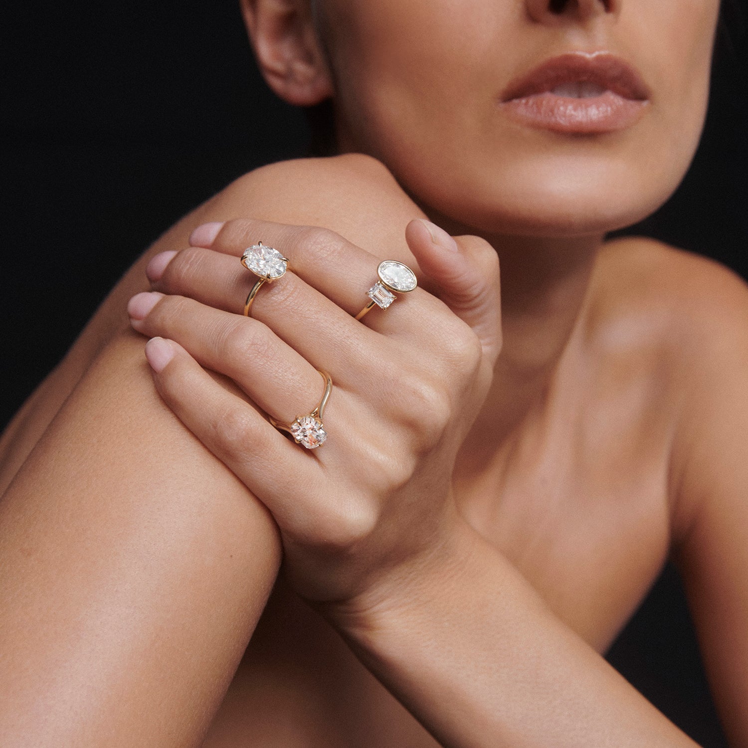 Woman showcases elegant gold rings with large diamond stones on her fingers, against a dark background. Perfect for luxury jewellery lovers.