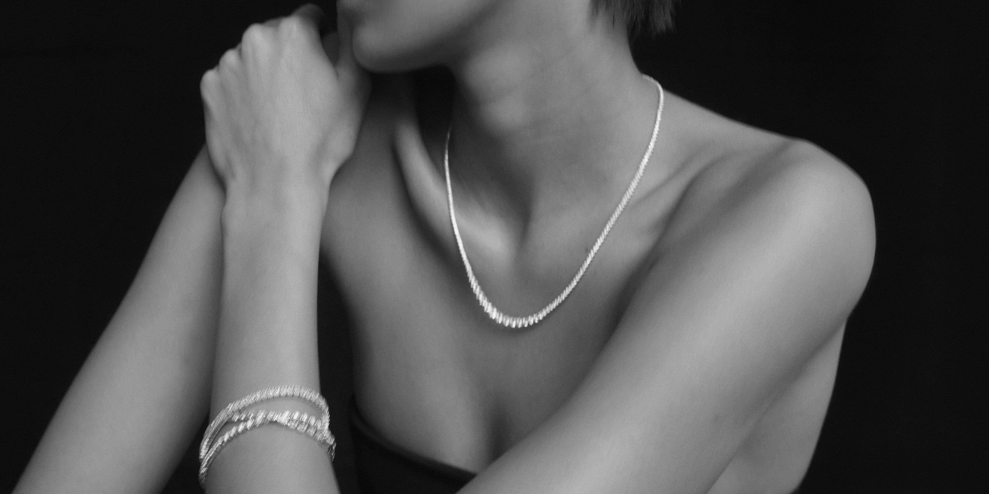 Model wearing elegant pearl necklace and bracelet against a black background, showcasing luxury jewellery style.