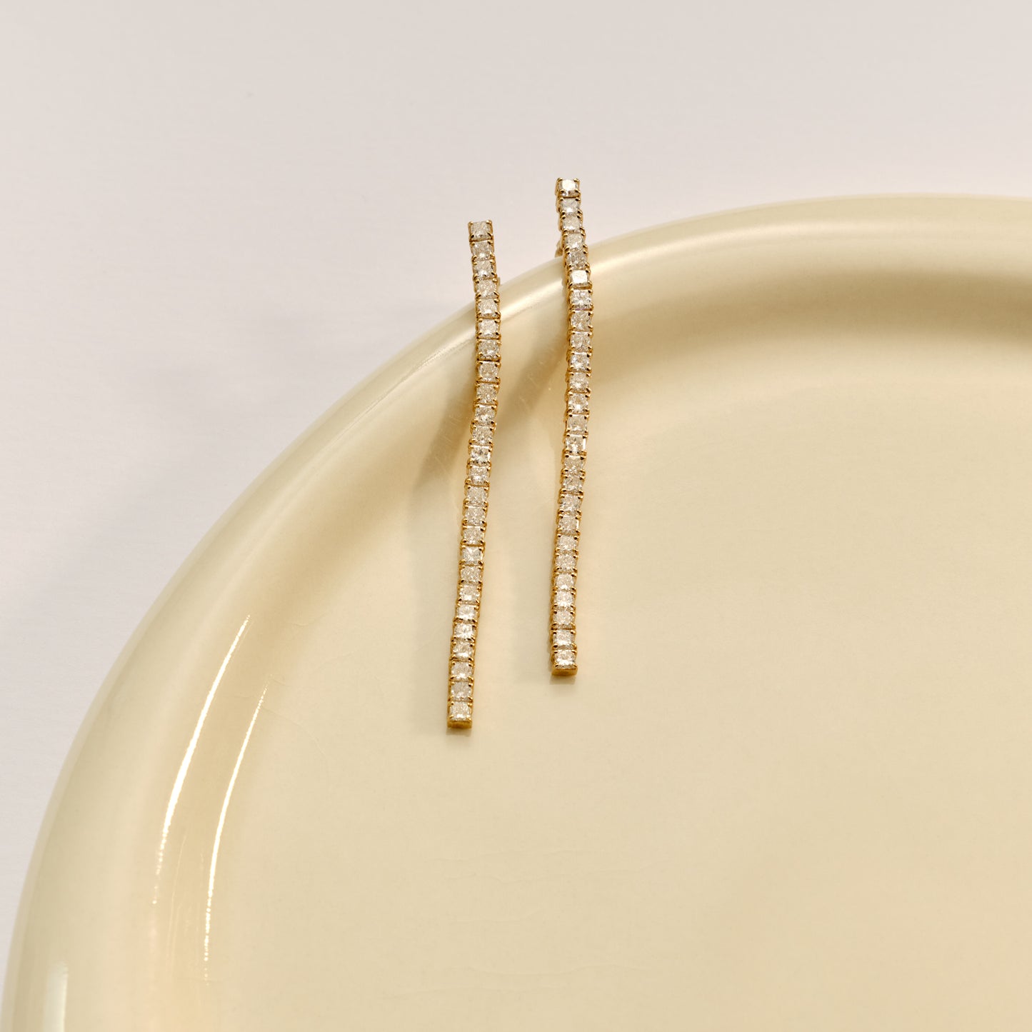 Elegant gold drop earrings with rows of sparkling diamonds, displayed on a pale, glossy ceramic surface. Luxurious jewellery.