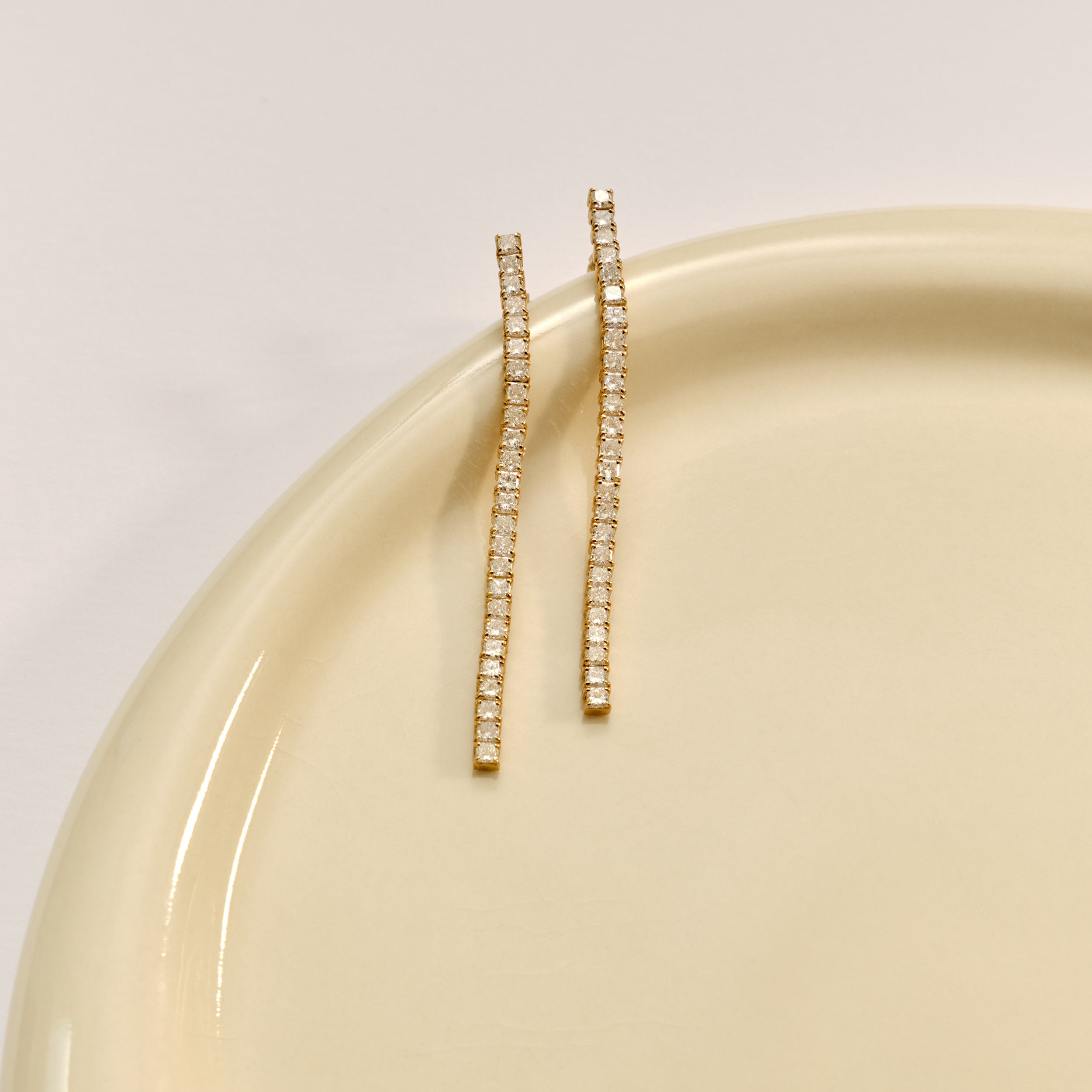 Elegant gold drop earrings with rows of sparkling diamonds, displayed on a pale, glossy ceramic surface. Luxurious jewellery.