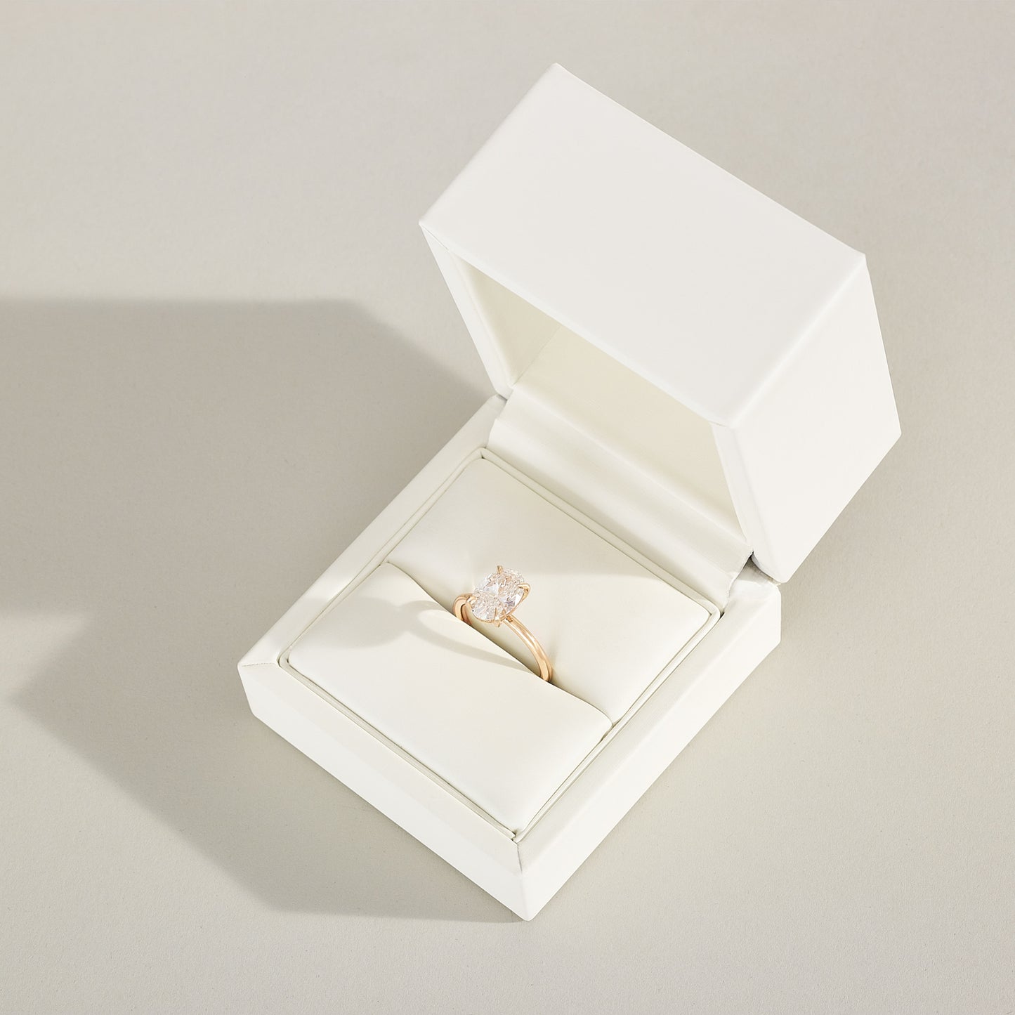 Gold ring with a diamond in an open white jewelry box on a light gray background