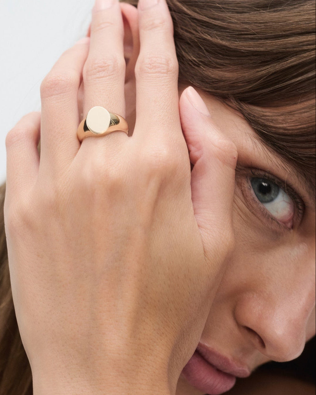 Woman wearing a gold ring on her finger with a plain background