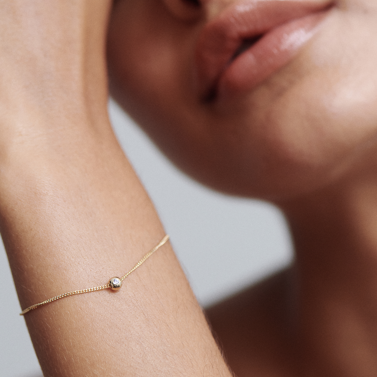 Close-up of a woman’s wrist with a delicate gold chain bracelet featuring a single diamond, set against her skin. Luxury jewellery elegance.