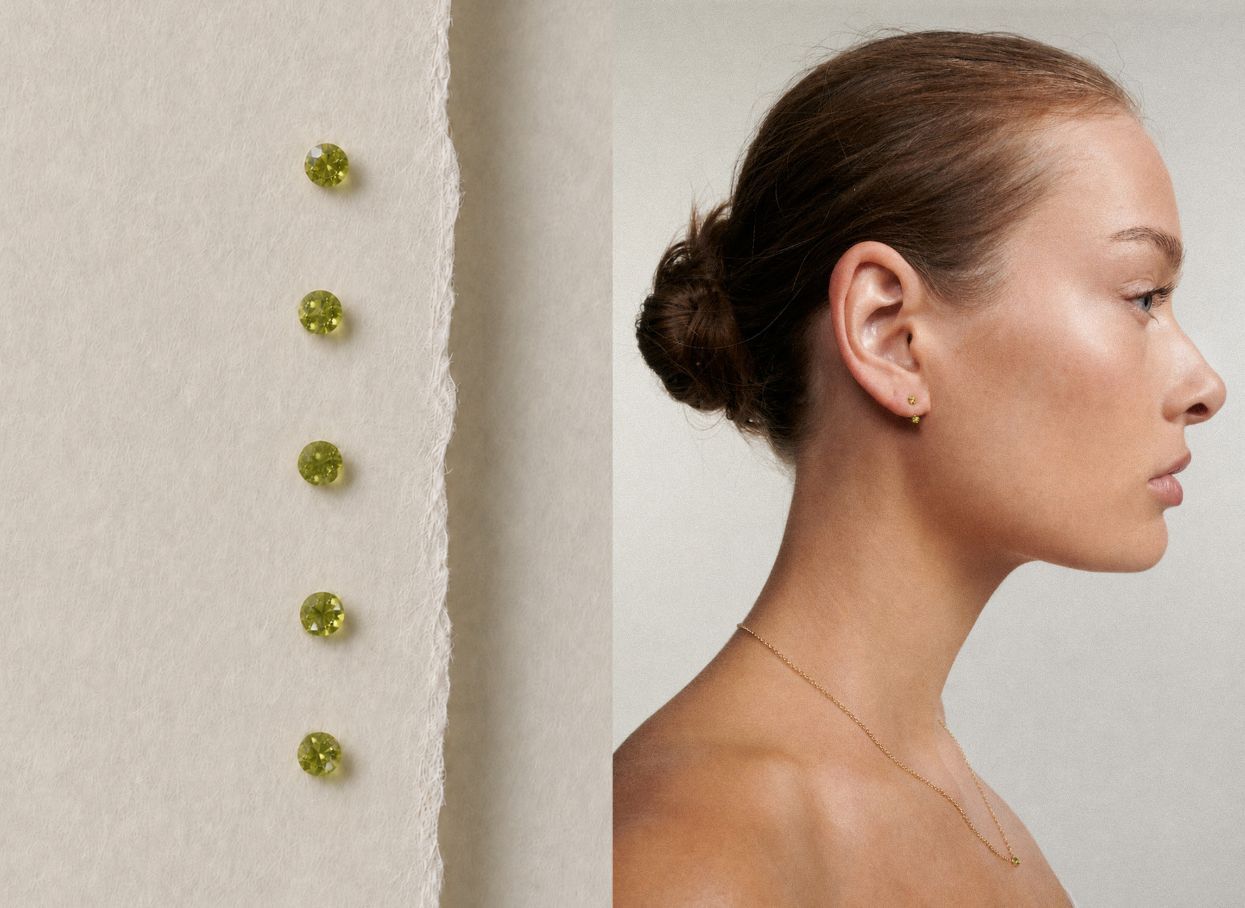A model in profile wearing a delicate gold necklace and a small gold stud earring, shown beside a close-up of five small round yellow-green gemstones on a textured off-white surface.