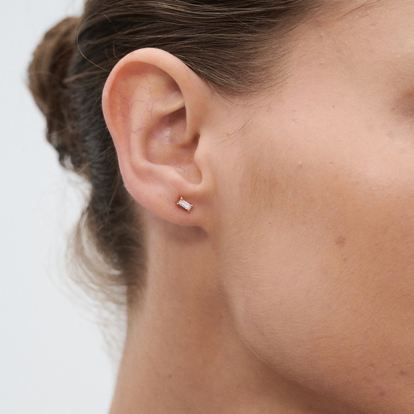 Close-up of a woman's ear adorned with a petite, rectangular diamond stud earring in a minimalist and luxurious jewellery design.