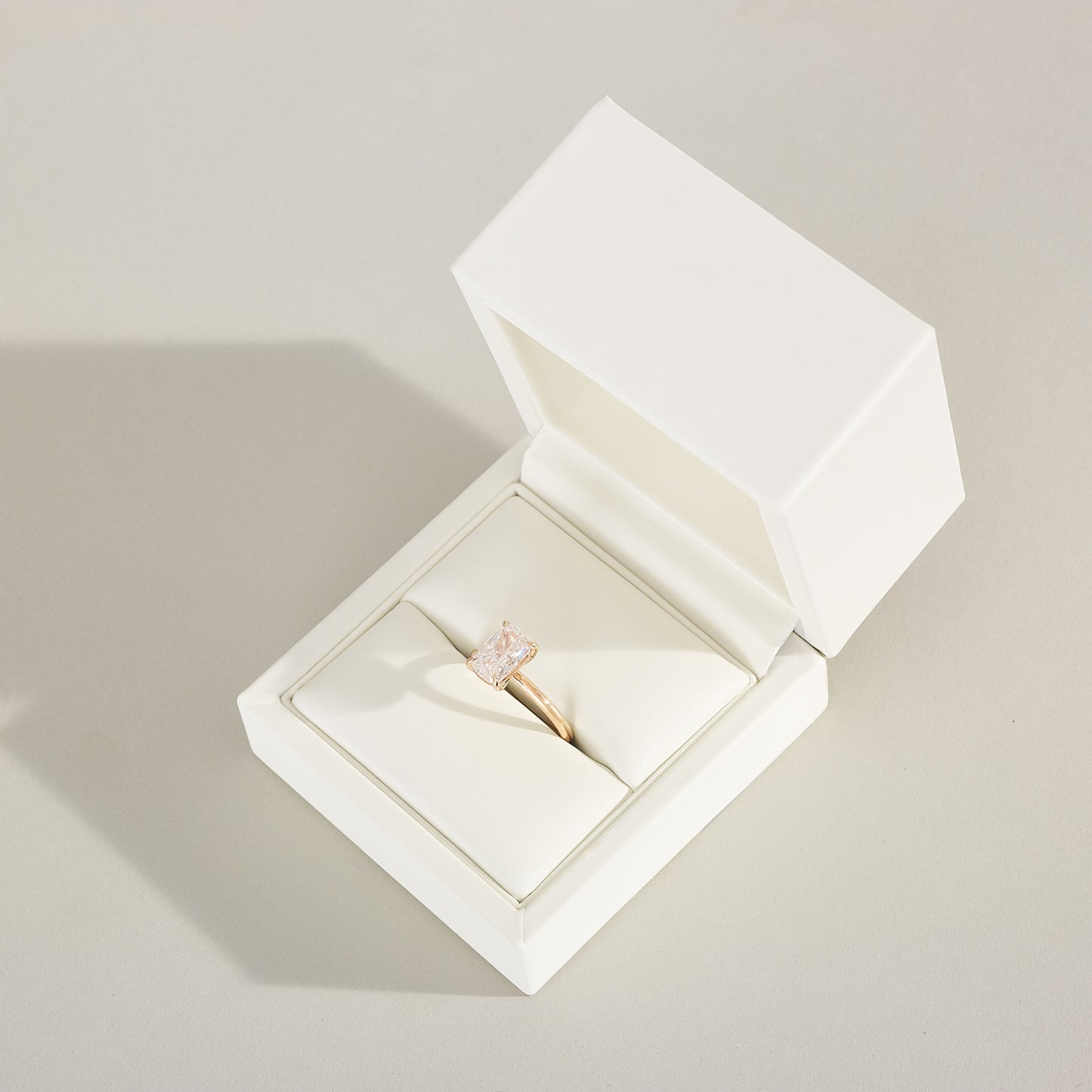 Gold ring with a diamond in an open white jewelry box on a light gray background