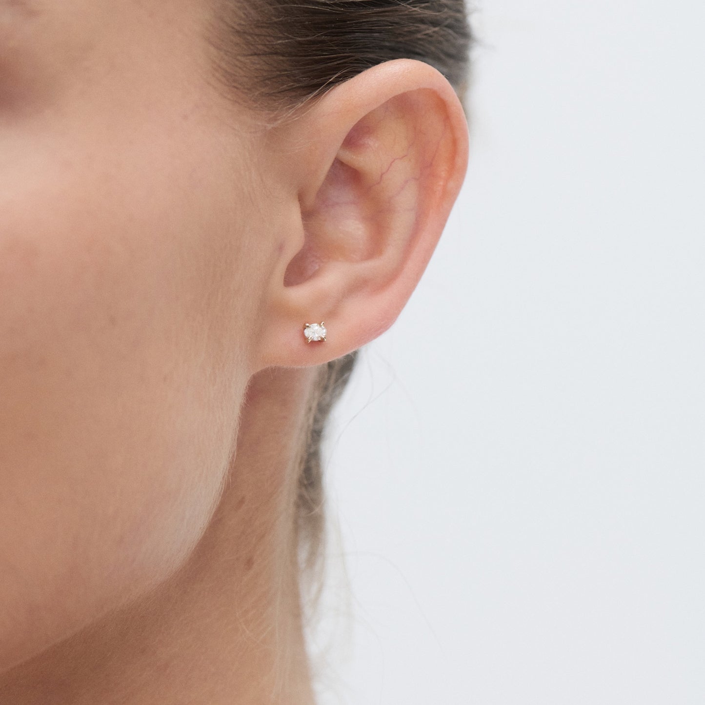 Close-up of a woman's ear wearing a single diamond stud earring. Perfect for highlighting simple, elegant jewellery design.