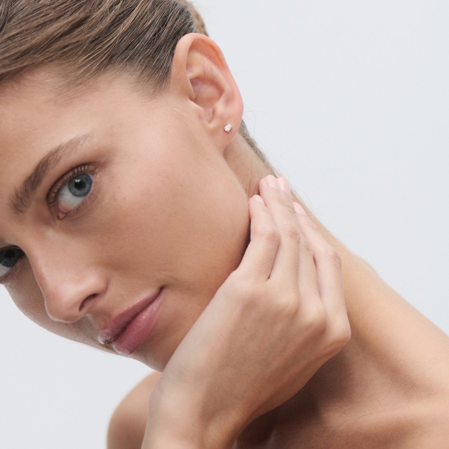 Woman with diamond stud earring, touching cheek. Elegant, minimalist jewellery in focus, soft background, luxury fashion accessory.