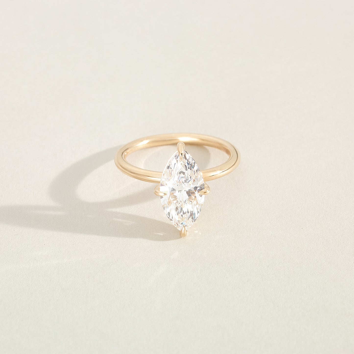 Gold ring with a pear-shaped diamond on a light beige background