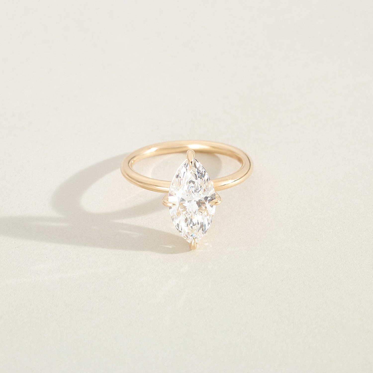 Gold ring with a pear-shaped diamond on a light beige background