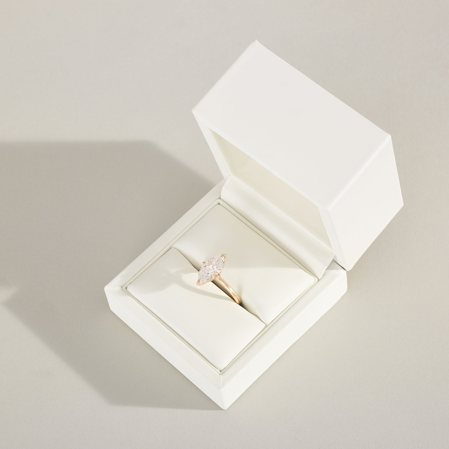 Gold ring with a diamond in an open white jewelry box on a light gray background