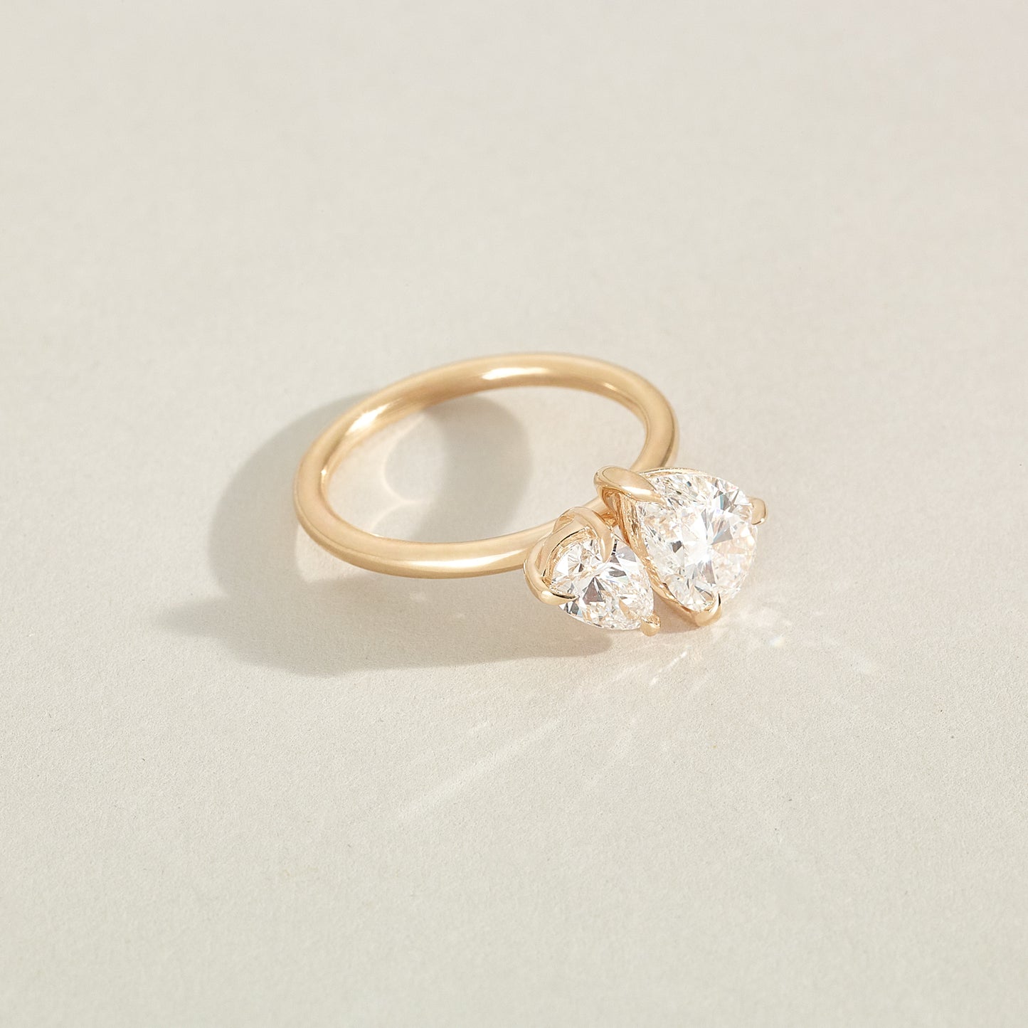 Gold ring with a heart-shaped diamond on a light beige background