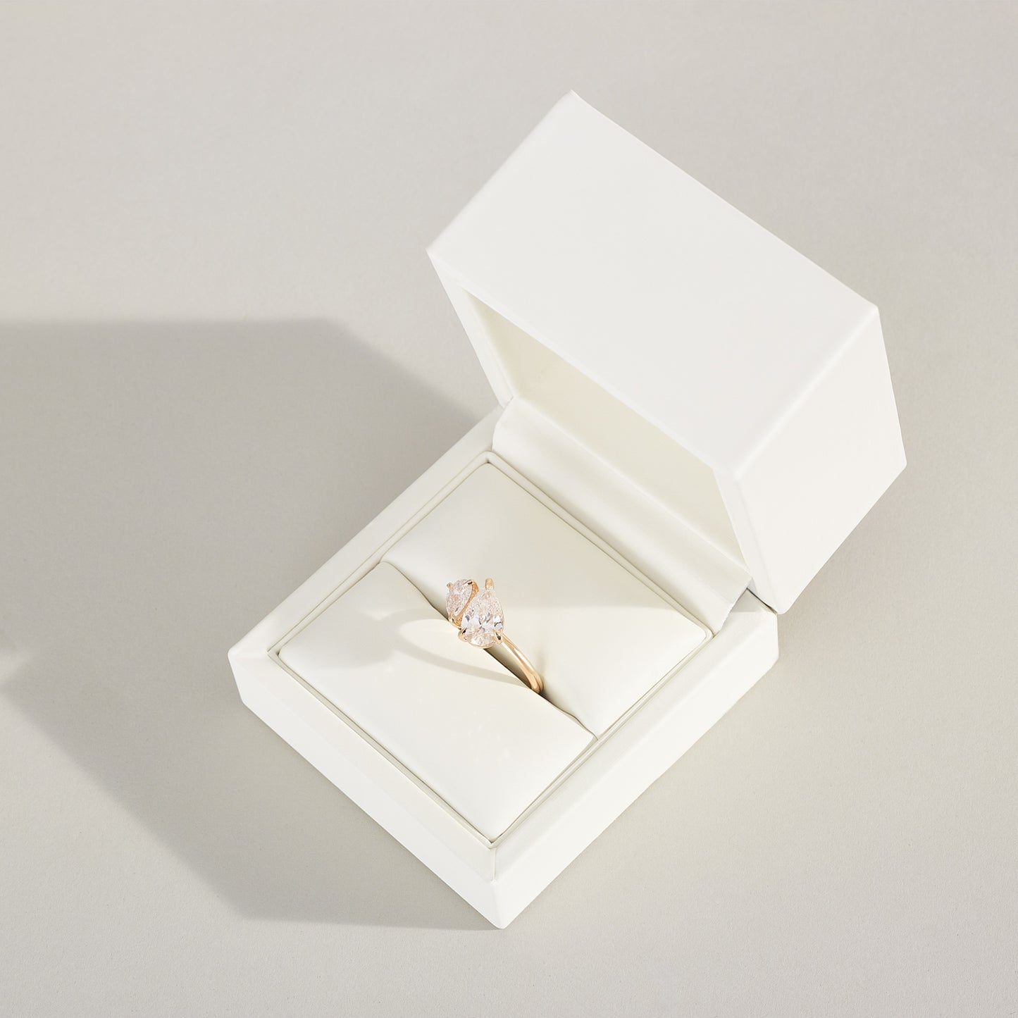 Diamond ring in an open white jewelry box on a light gray background