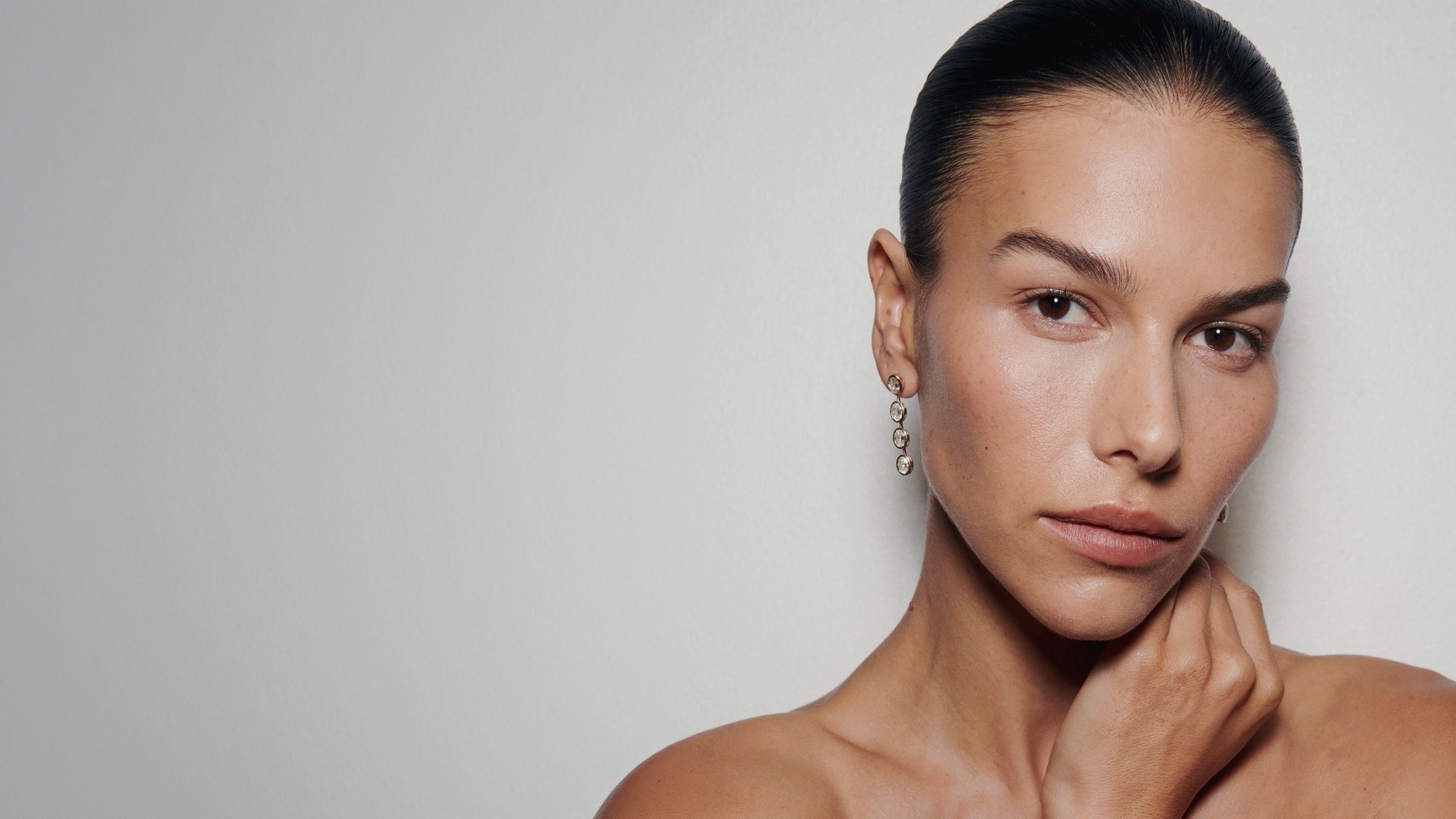 Close-up portrait of a woman wearing oval bezel diamond drop earrings.