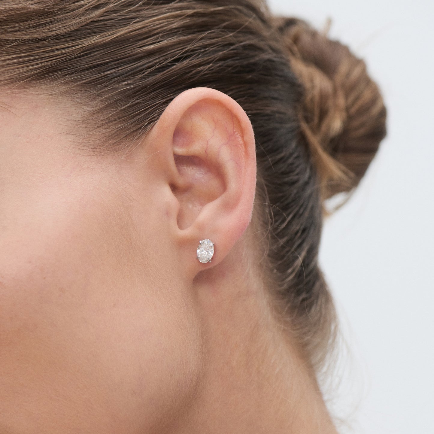 Close-up of a woman's ear wearing an elegant diamond stud earring. Hair is styled in a bun, showcasing the jewellery.
