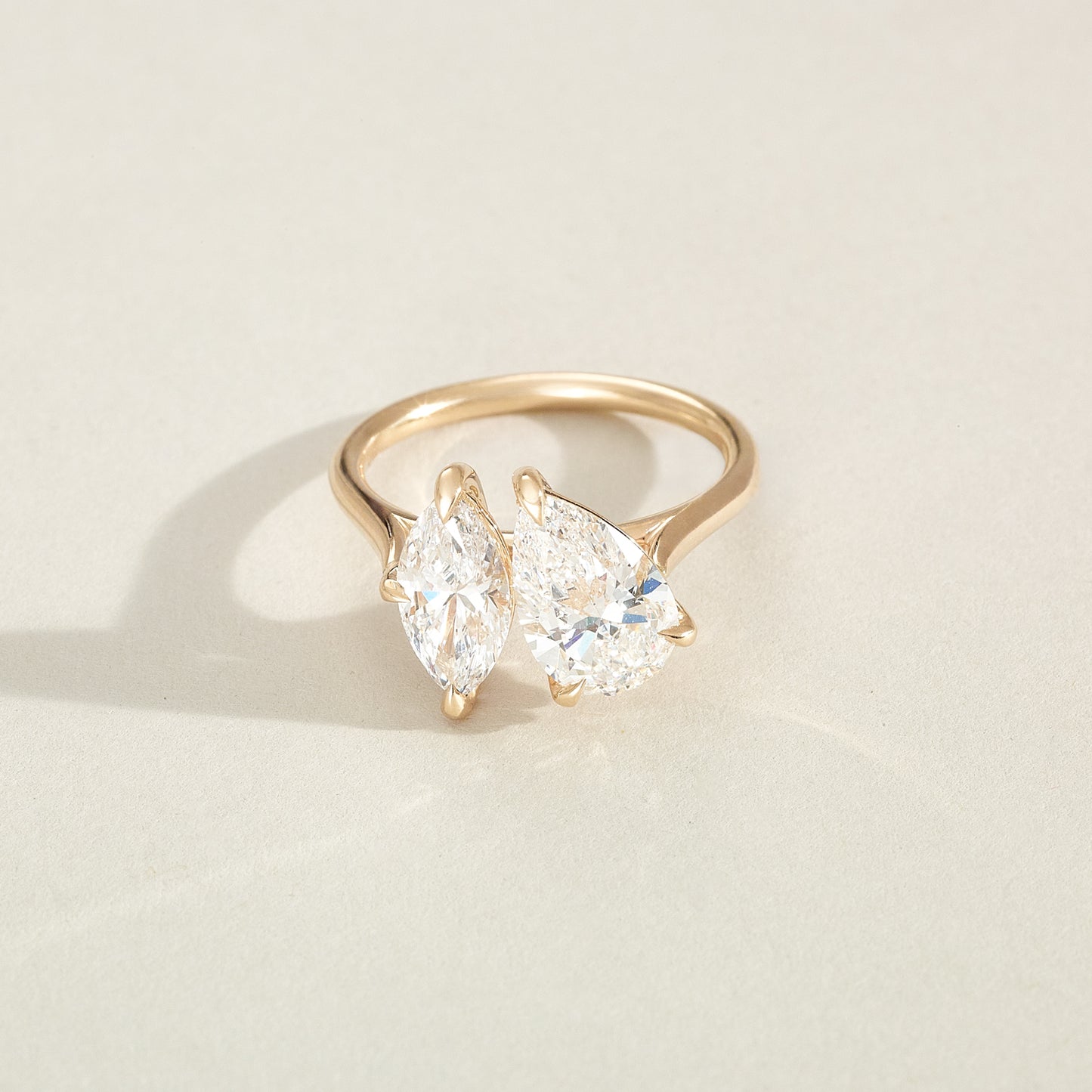 Gold ring with two pear-shaped diamonds on a light beige background