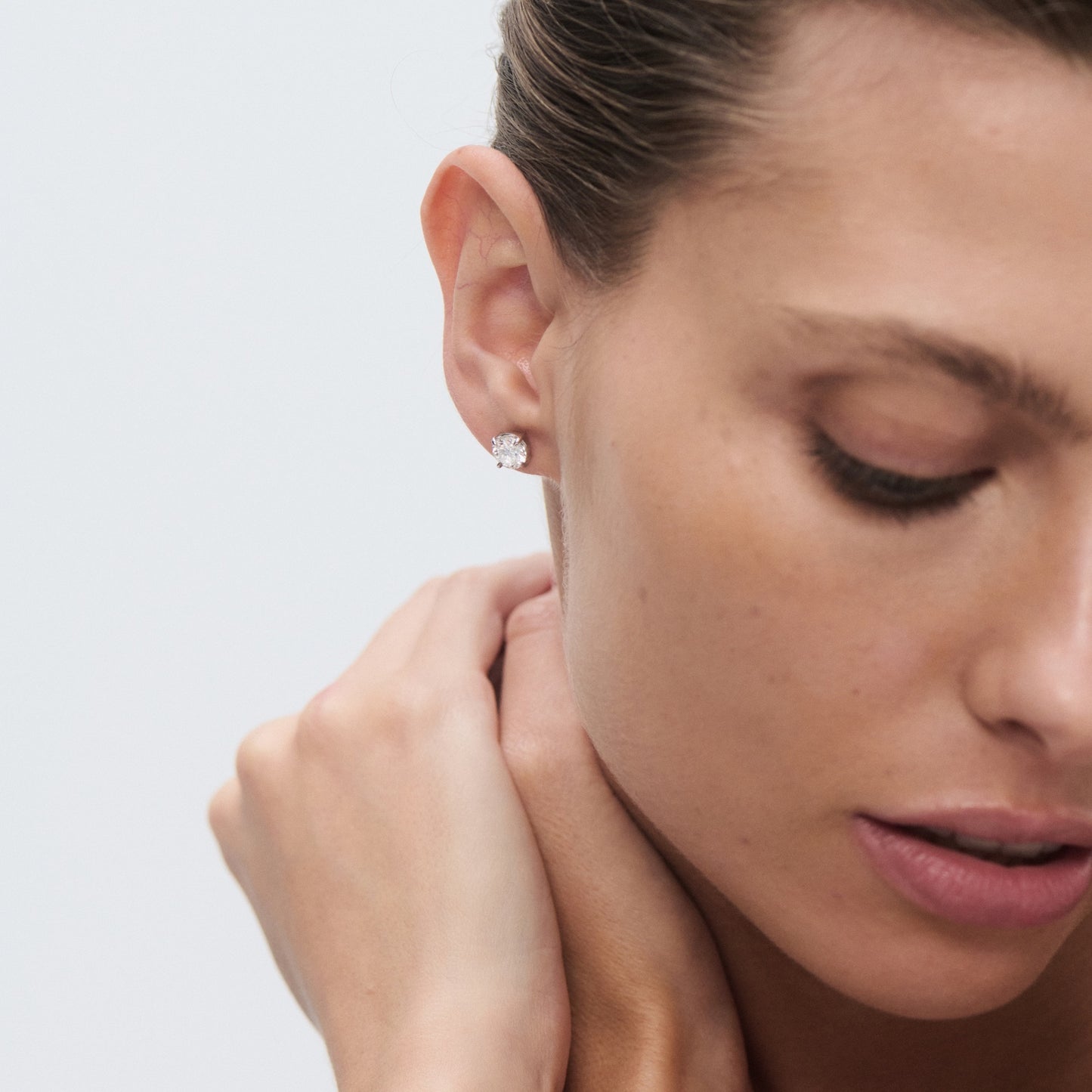 Woman wearing a single solitaire diamond stud earring, with a serene expression, neck slightly bent, and hair tied back.