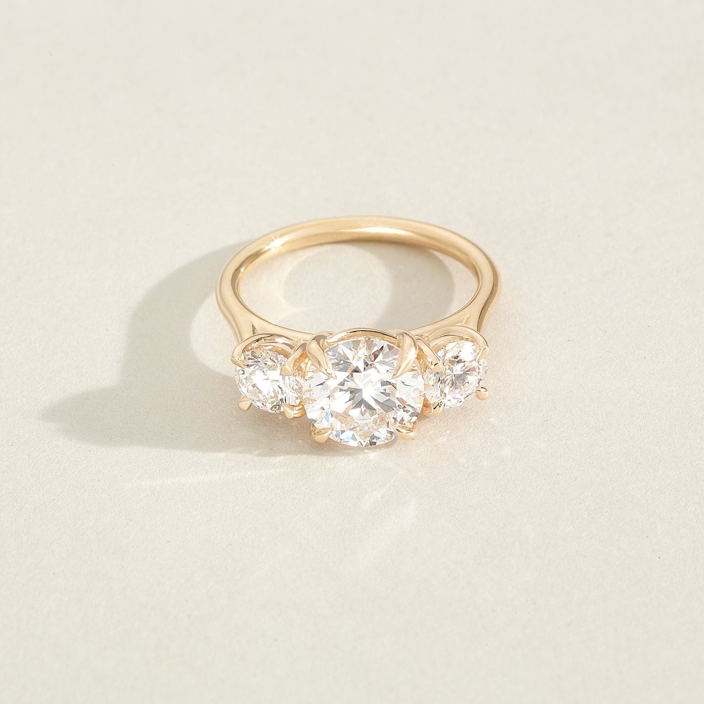 Gold ring with three diamonds on a light beige background