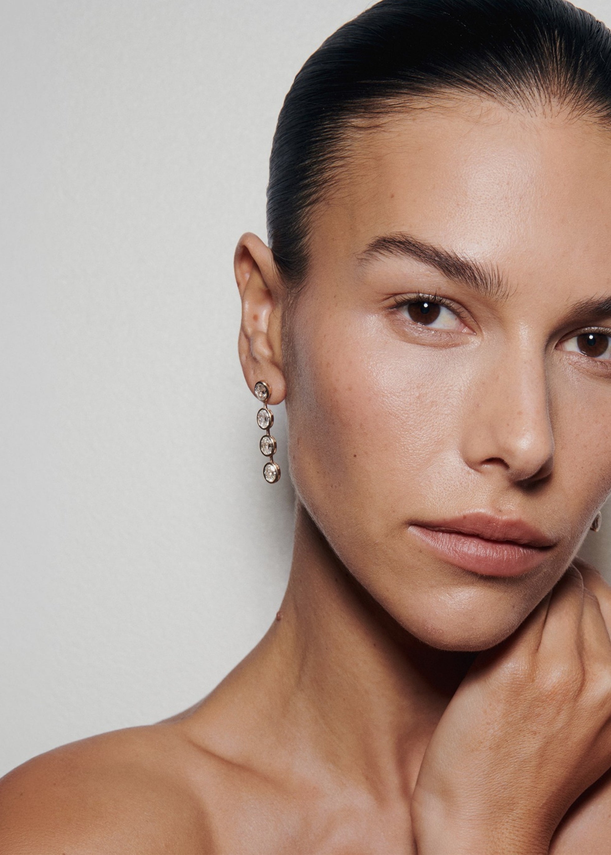 Close-up portrait of a woman wearing oval bezel diamond drop earrings.