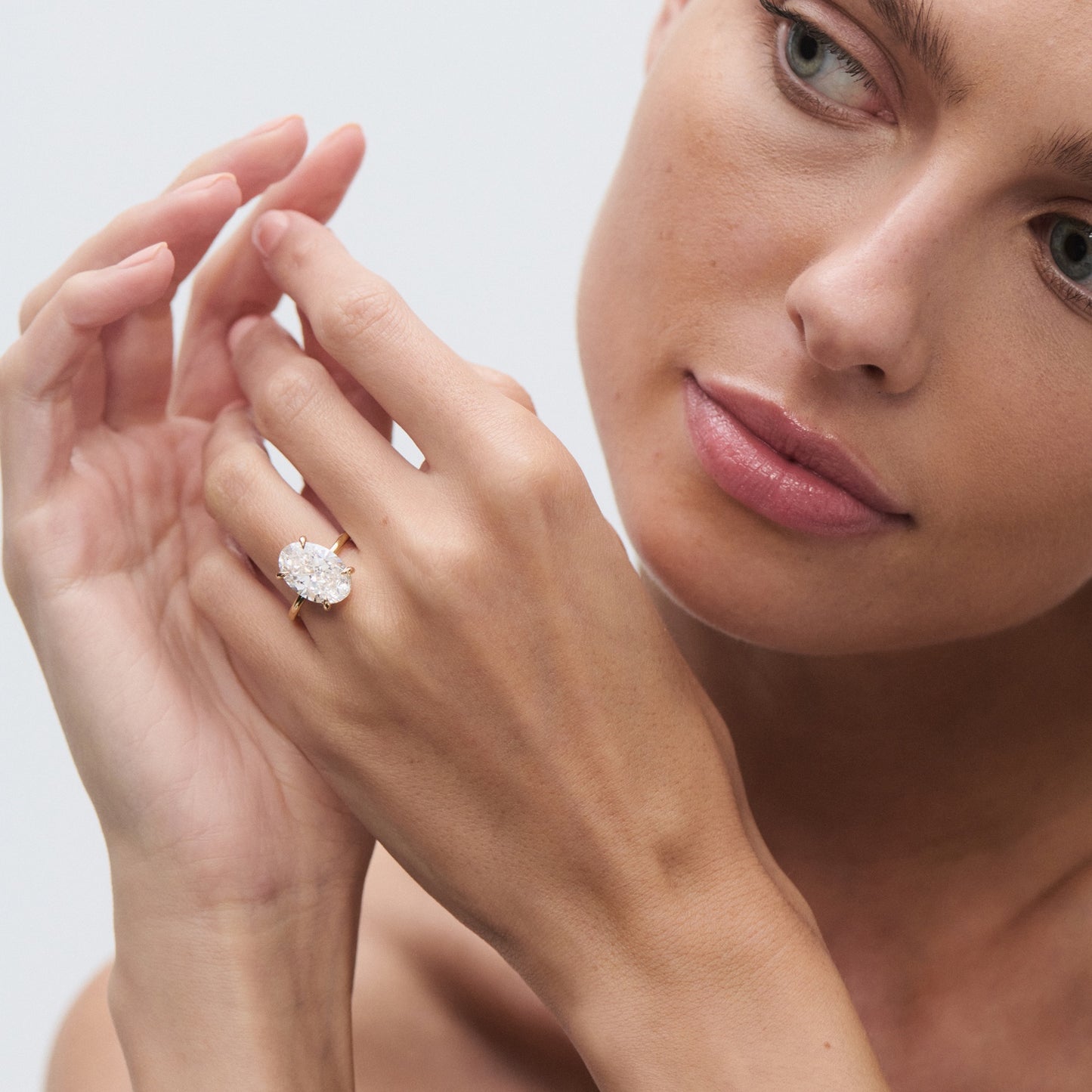 Woman admiring her hand with a large oval diamond ring, showcasing luxury jewellery on a light background.