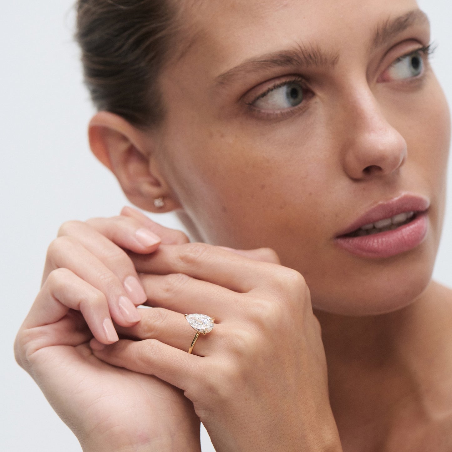 Woman with an elegant diamond ring on her finger, gazing to the side. Luxurious jewellery focus, subtle makeup, and neat manicure.