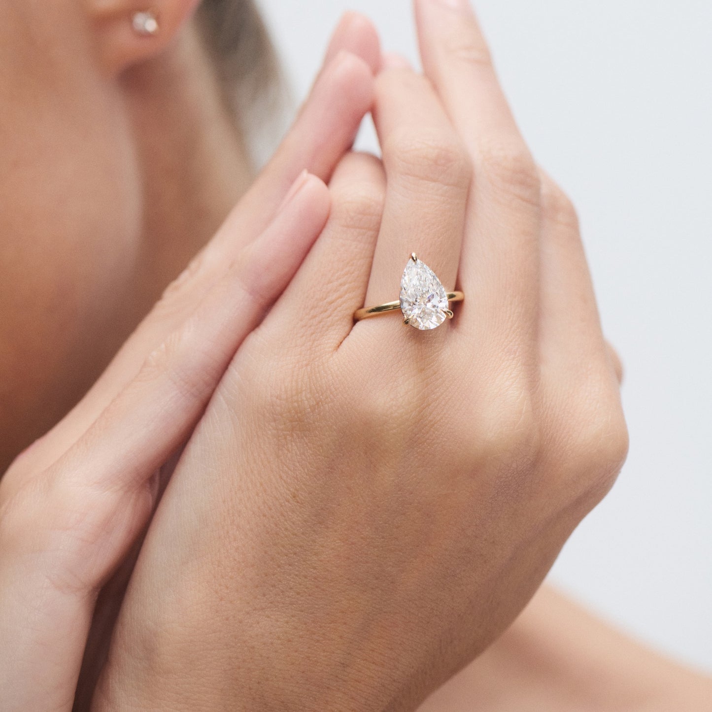 Close-up of a hand wearing a pear-shaped diamond ring on a gold band, highlighting luxury jewellery.