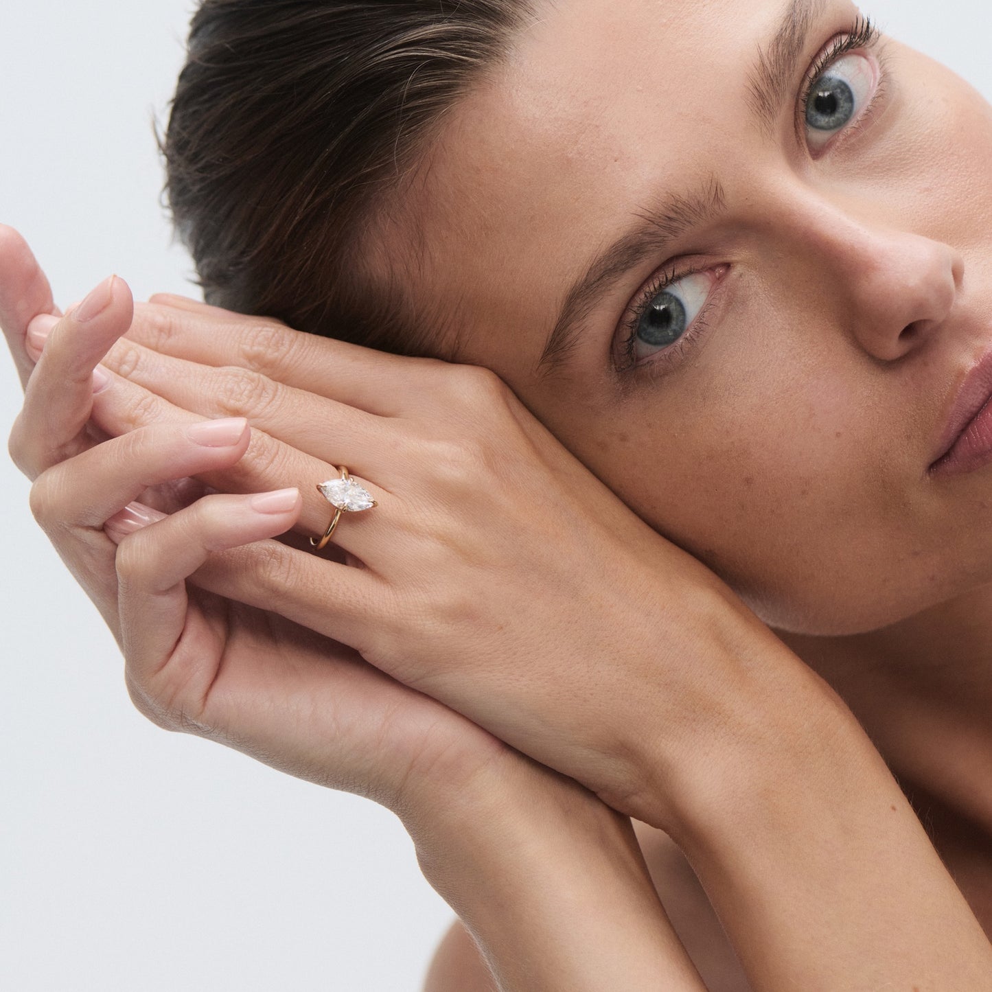 Woman showcasing a marquise-cut diamond ring on her finger, resting her face against her hands. Luxury jewellery, elegant style.