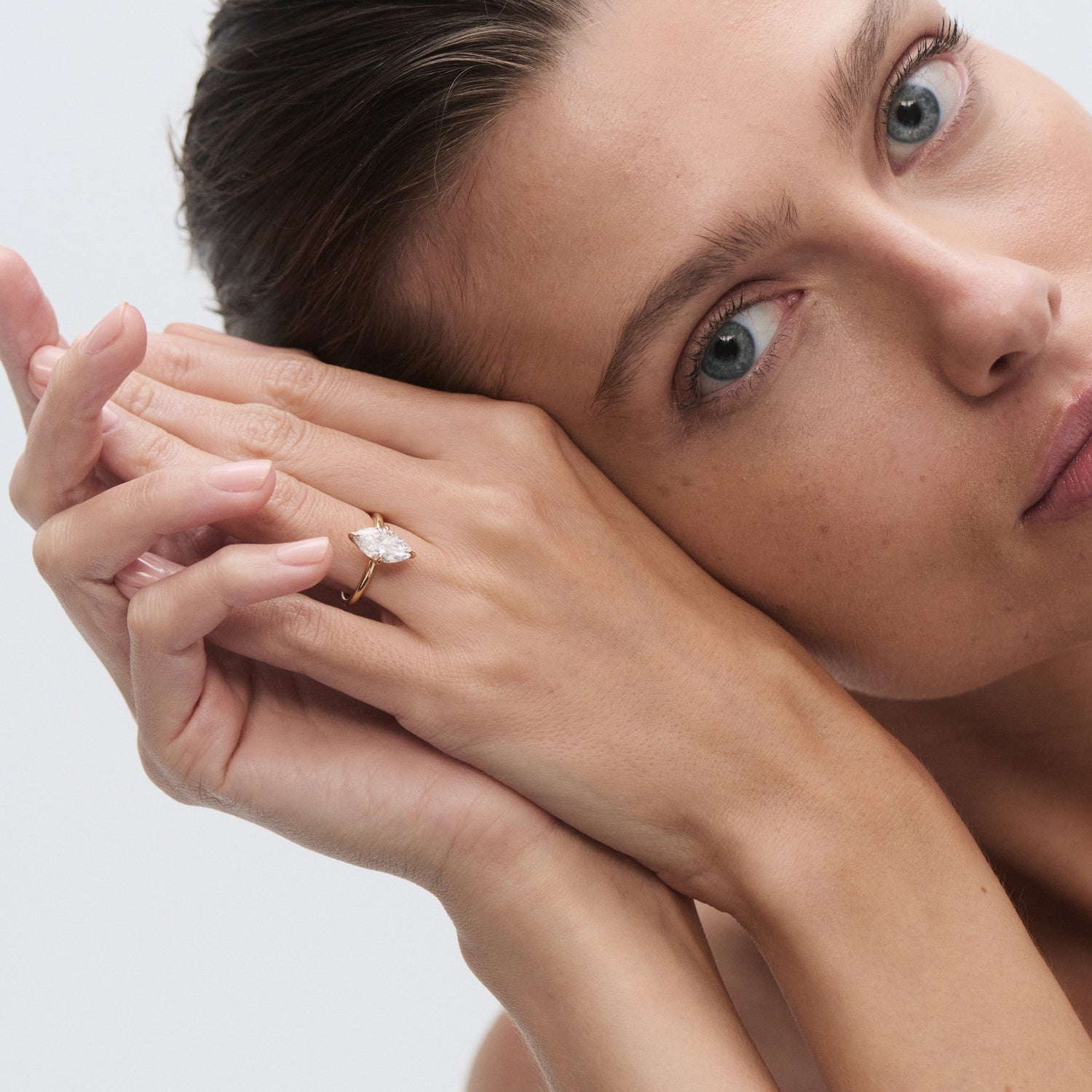 Woman showcasing a marquise-cut diamond ring on her finger, resting her face against her hands. Luxury jewellery, elegant style.